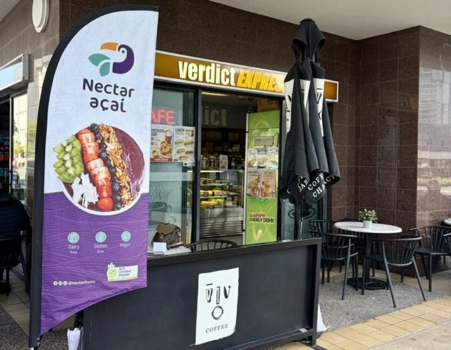 Street view of Verdict Espresso coffee shop and cafe showing outside tables and chairs and a large colourful acai banner.