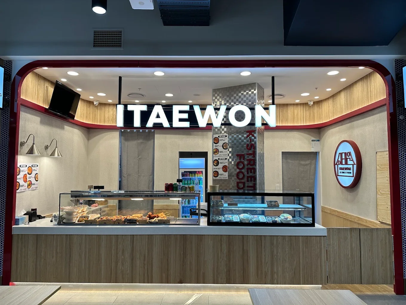Korean restaurant named 'Taewon' with a display counter of food and beverages, illuminated sign, and seating area.