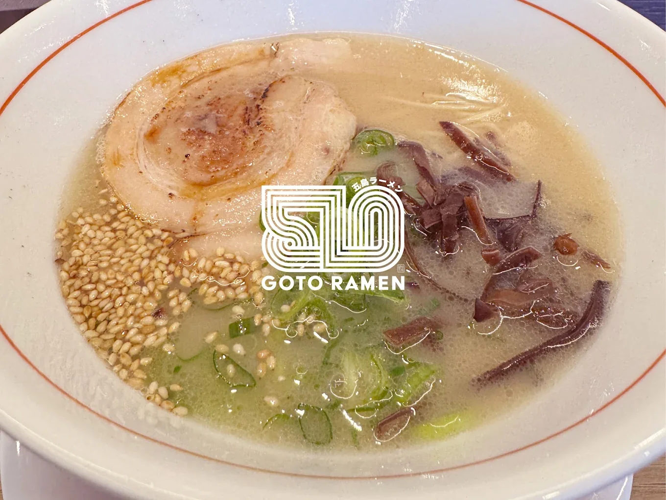 Bowl of ramen with pork, seaweed, green onions, sesame seeds, and broth, featuring a "50 GOTO RAMEN" logo in the center.