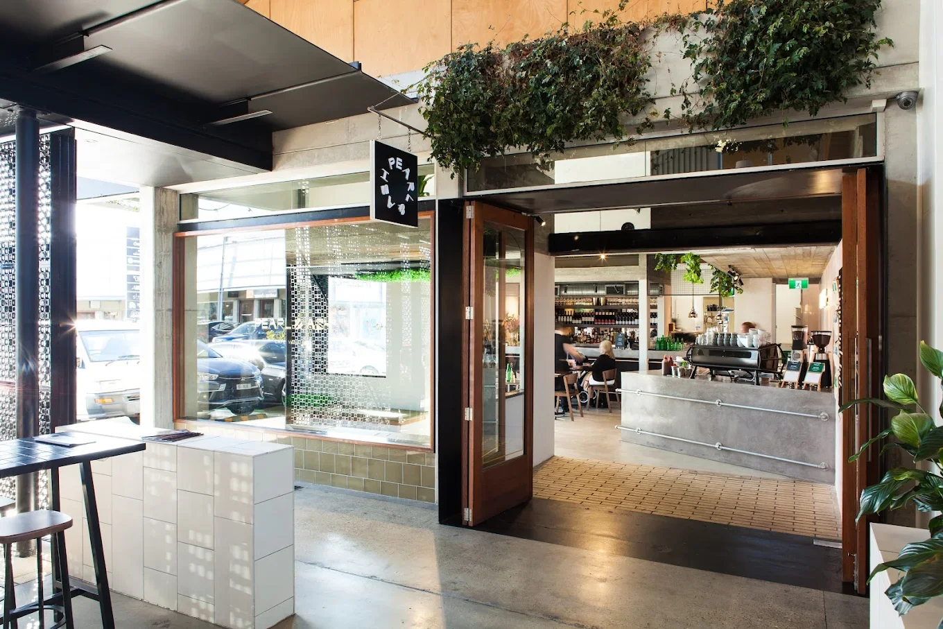 View of the front of Pearl & Ash Cafe, Brickworks Southport. Modern glass and wood frontage with foliage.