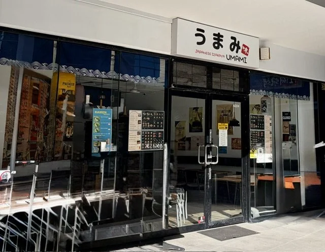 View of front of Japanese restaurant 'IZAKAYA UMANI' in Southport with it's glass front and sign-box above the glass doors.