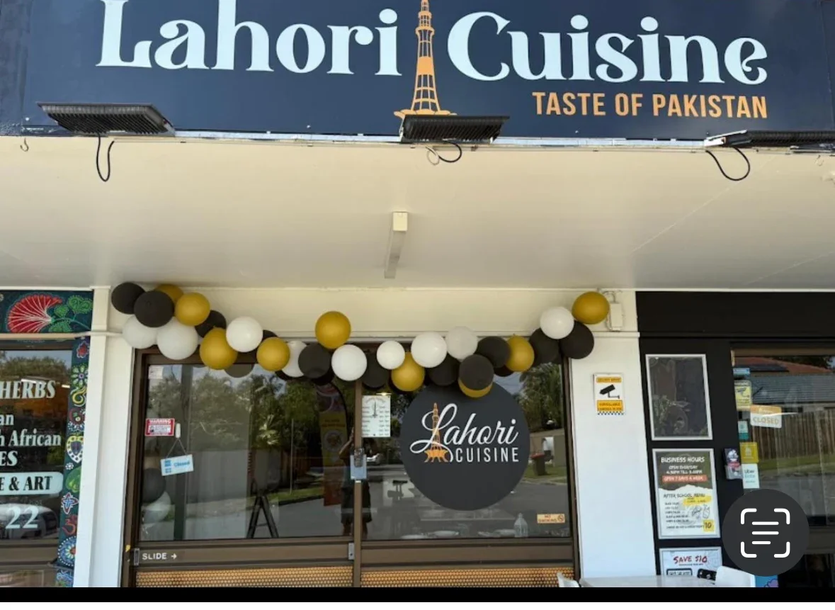 The storefront of Lahori Cuisine, a Pakistani restaurant, with black, white, and gold balloons decorating the entrance and a sign that reads 'Lahori Cuisine'.
