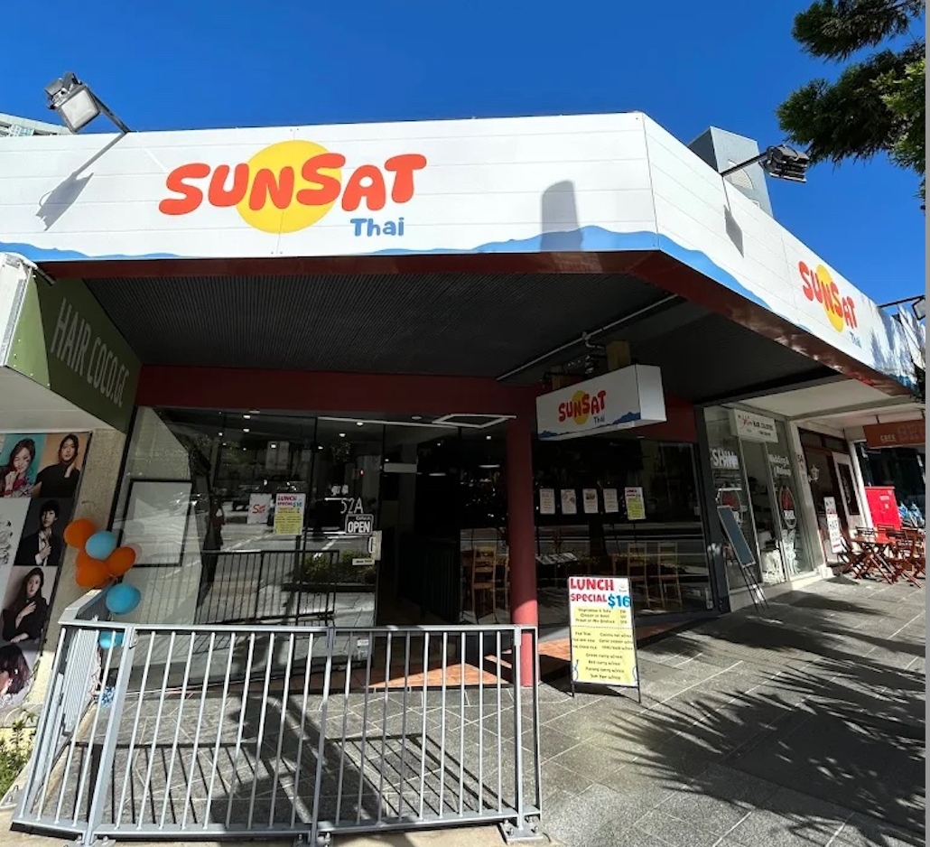 Exterior view of a restaurant named Sunsat Thai with a white awning, logo in red and yellow, and sidewalk seating.