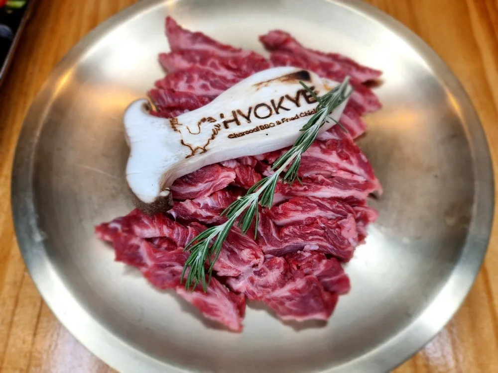 Sliced raw beef with a sprig of rosemary and a mushroom that has the word 'HOKY' branded on it, placed on a metal tray.