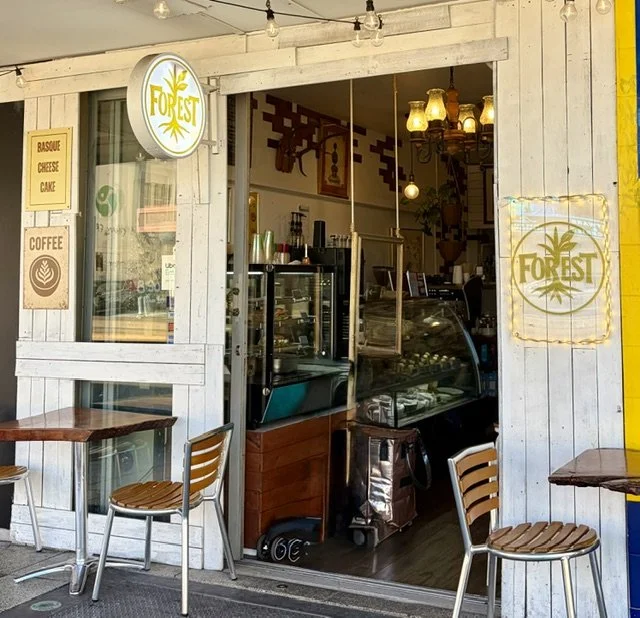 View of outside and through the front door of dessert cafe 'Forest' with tables and chairs either side on the outside along with the Forest signage, also some glass display cabinets within.