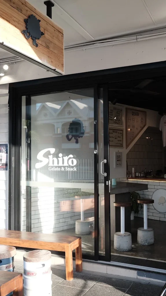 Exterior view of Shiro Gelato & Snack shop with glass door and wooden accents, displaying the shop logo and interior seating.