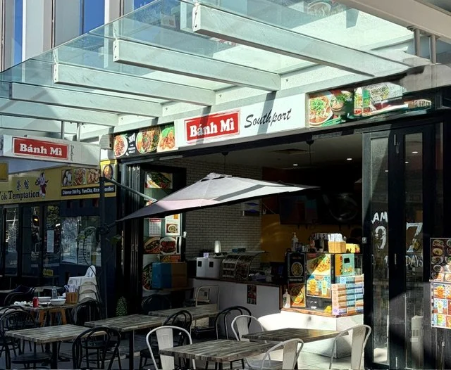 Front view of 'Bahn Mi" Vietnamese in Southport Central showing outside tables and chairs with umbrellas and the front counter.