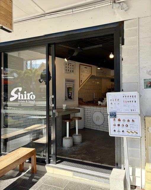 Exterior view of Shiro Gelato & Snack shop with glass door and wooden accents, displaying the shop logo and interior seating.