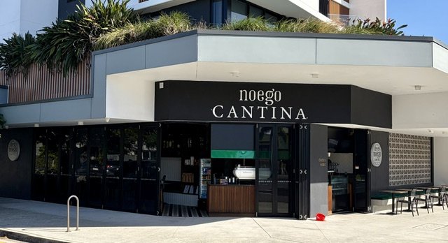 Street view of modern cafe Noego Cantina in Southport showing large signage across front and some tables and chairs.