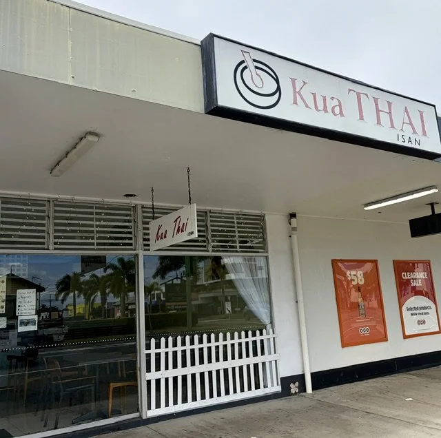 Kua Thai restaurant street view showing signage and glass front with white picket fence mural.