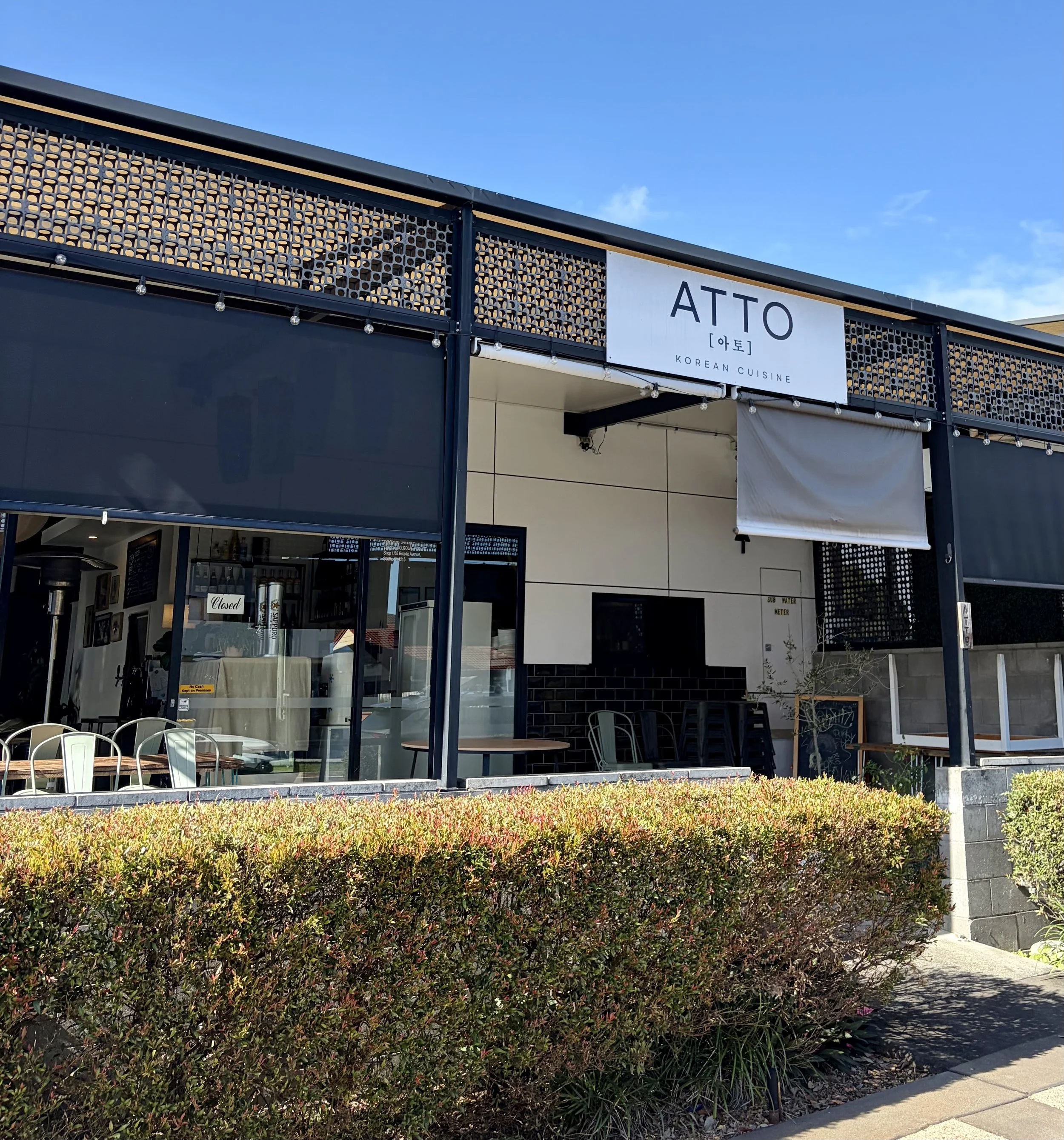 Modern front of Korean restaurant ATTO with black signage on white background. The sign is on a black meshed background.