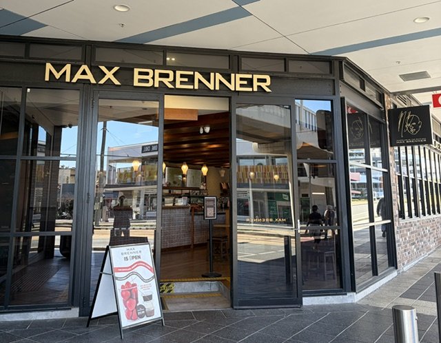 Front entry view of Max Brenner Chocolate House in Southport. Modern new shopfront in deep browns and gold.