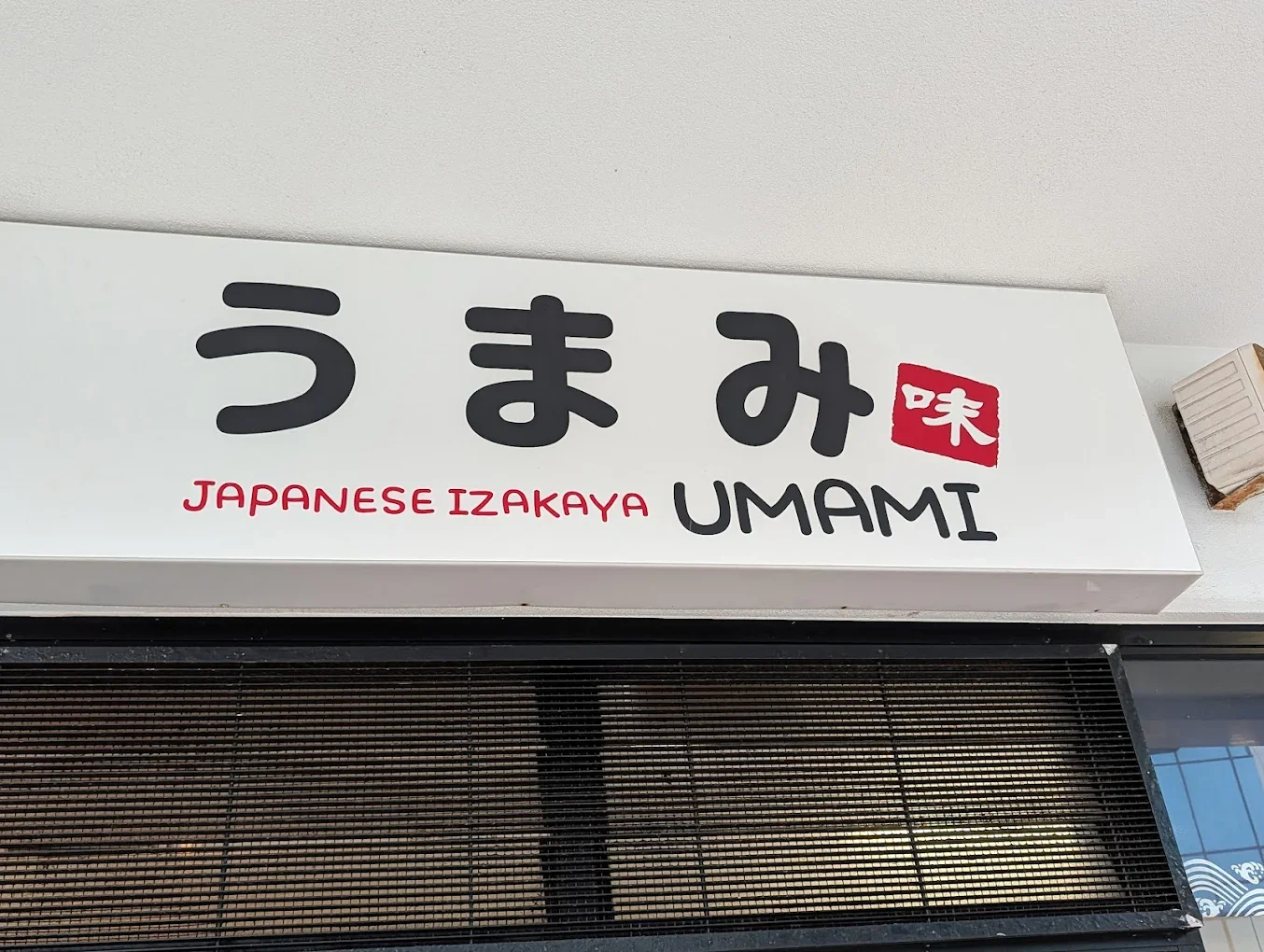 Sign for Japanese Izakaya restaurant named Umami with Japanese characters and red stamp.