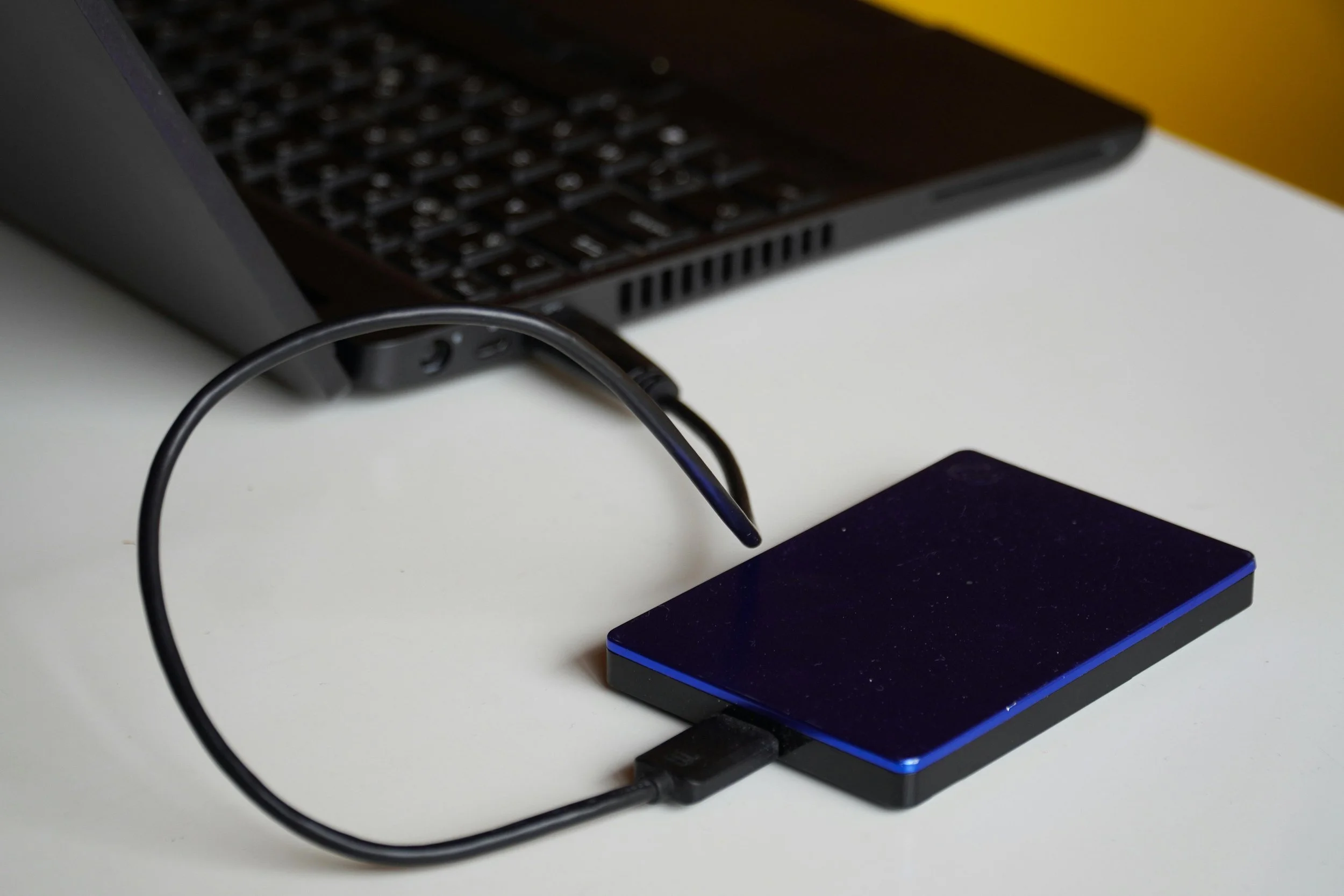 Disque dur externe connecté à un ordinateur portable par un câble USB sur une table blanche.