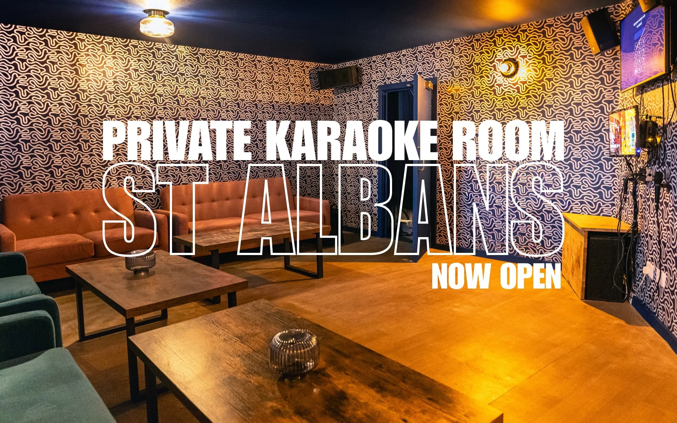 Interior of a decorated private karaoke room with patterned walls, plush seating, coffee tables, and wall-mounted screens.
