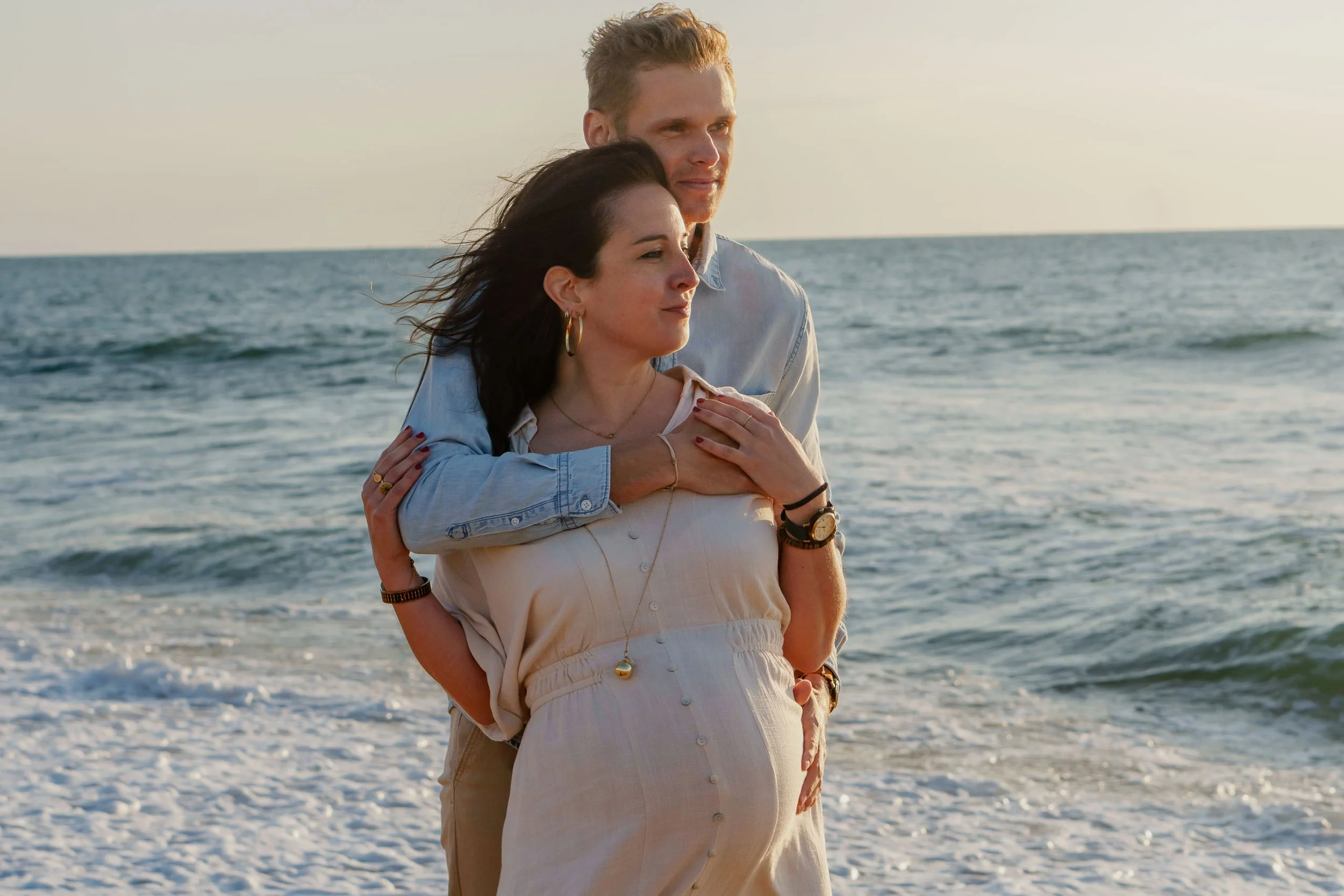 Un couple qui se serre dans les bras sur la plage au coucher du soleil, avec l'océan en arrière-plan.