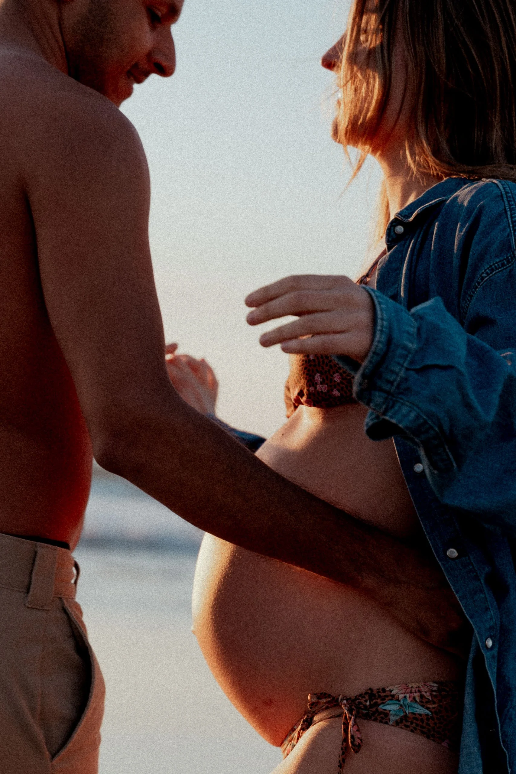 Deux personnes debout très proches, probablement un couple, avec un fond de ciel au coucher du soleil, partageant un moment intime sur la plage.