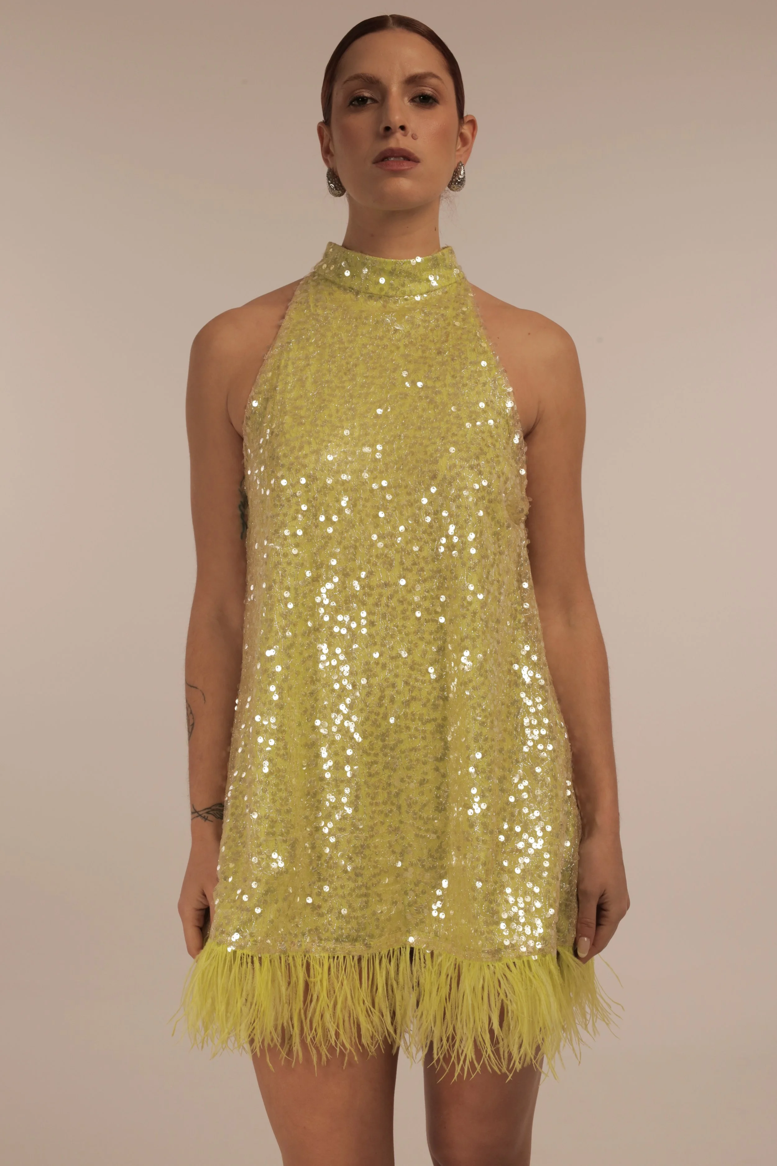 A woman in a yellow, sequined dress with a feathered hemline and a high neckline, standing against a plain background.