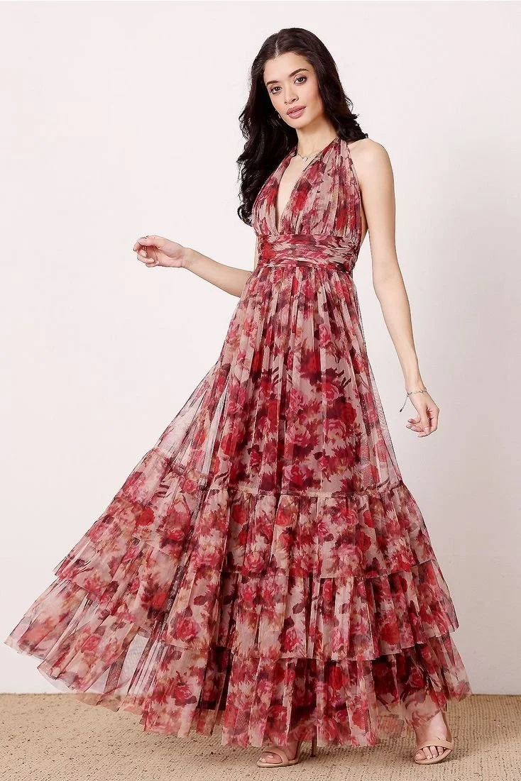 Woman in a sleeveless, floral, red and pink maxi dress with layered skirt, standing against a plain background.