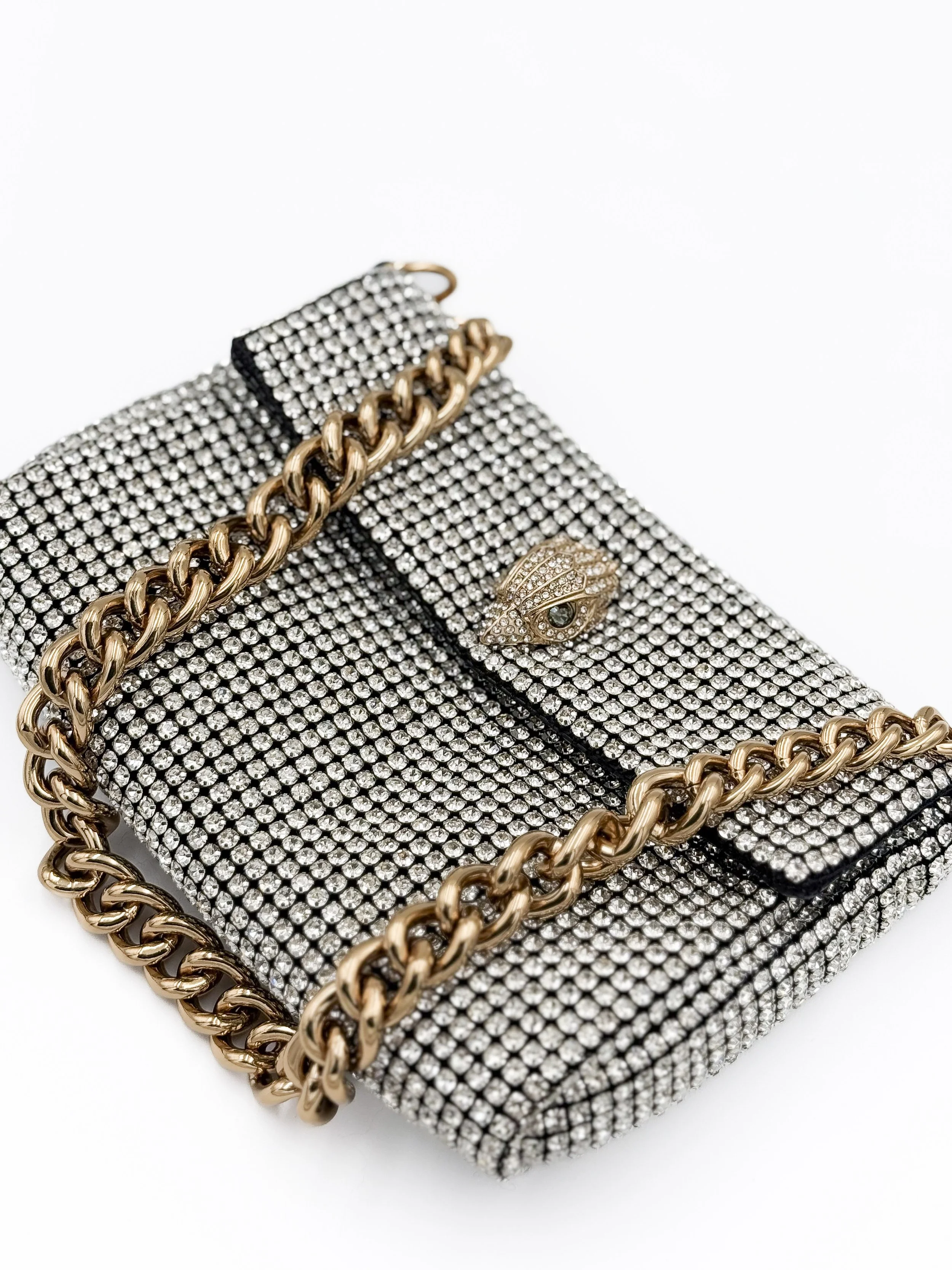 A jewel-encrusted clutch purse with a gold chain handle and decorative gold eye-shaped embellishment.