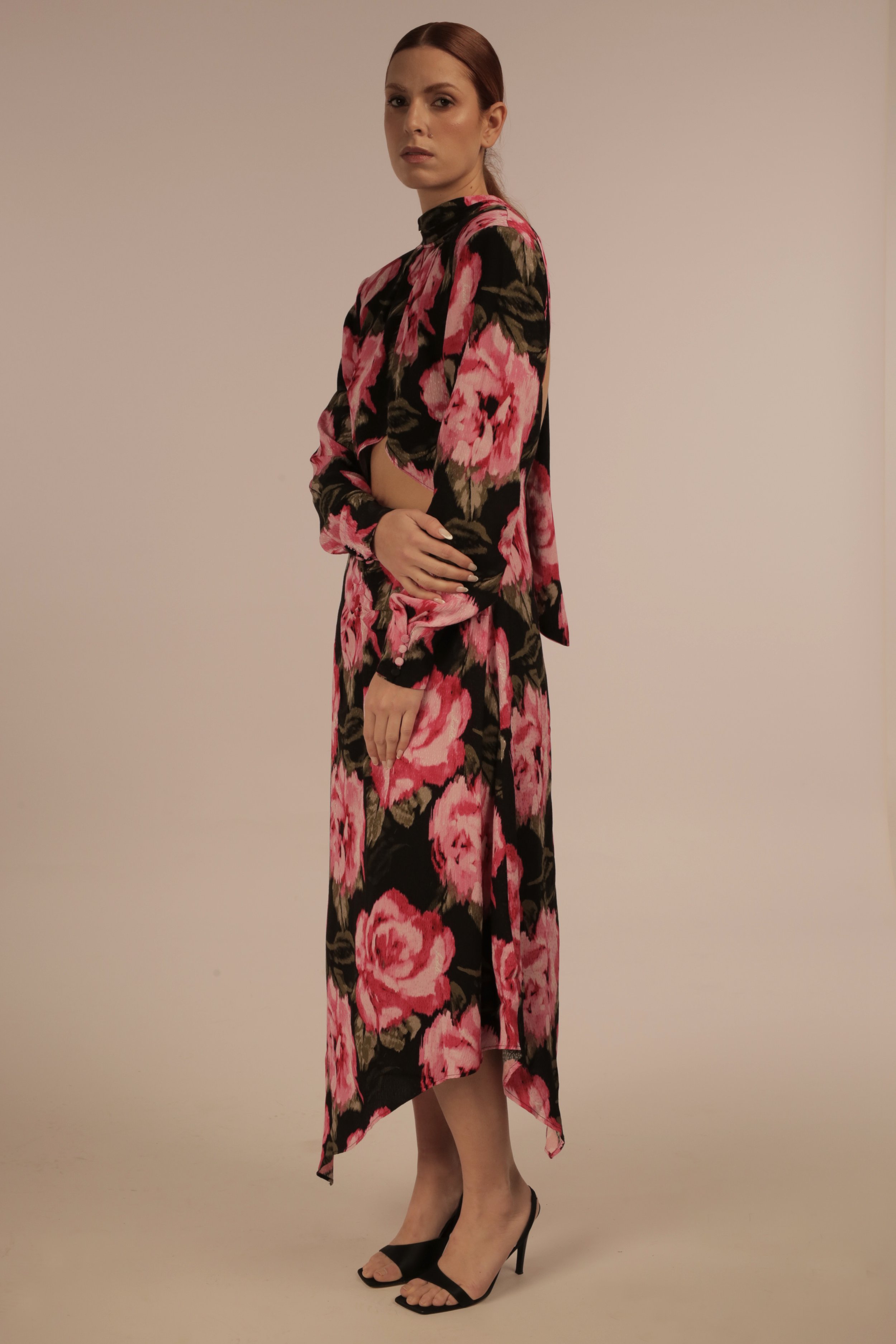 A woman in a floral outfit with black high heels standing against a plain background.