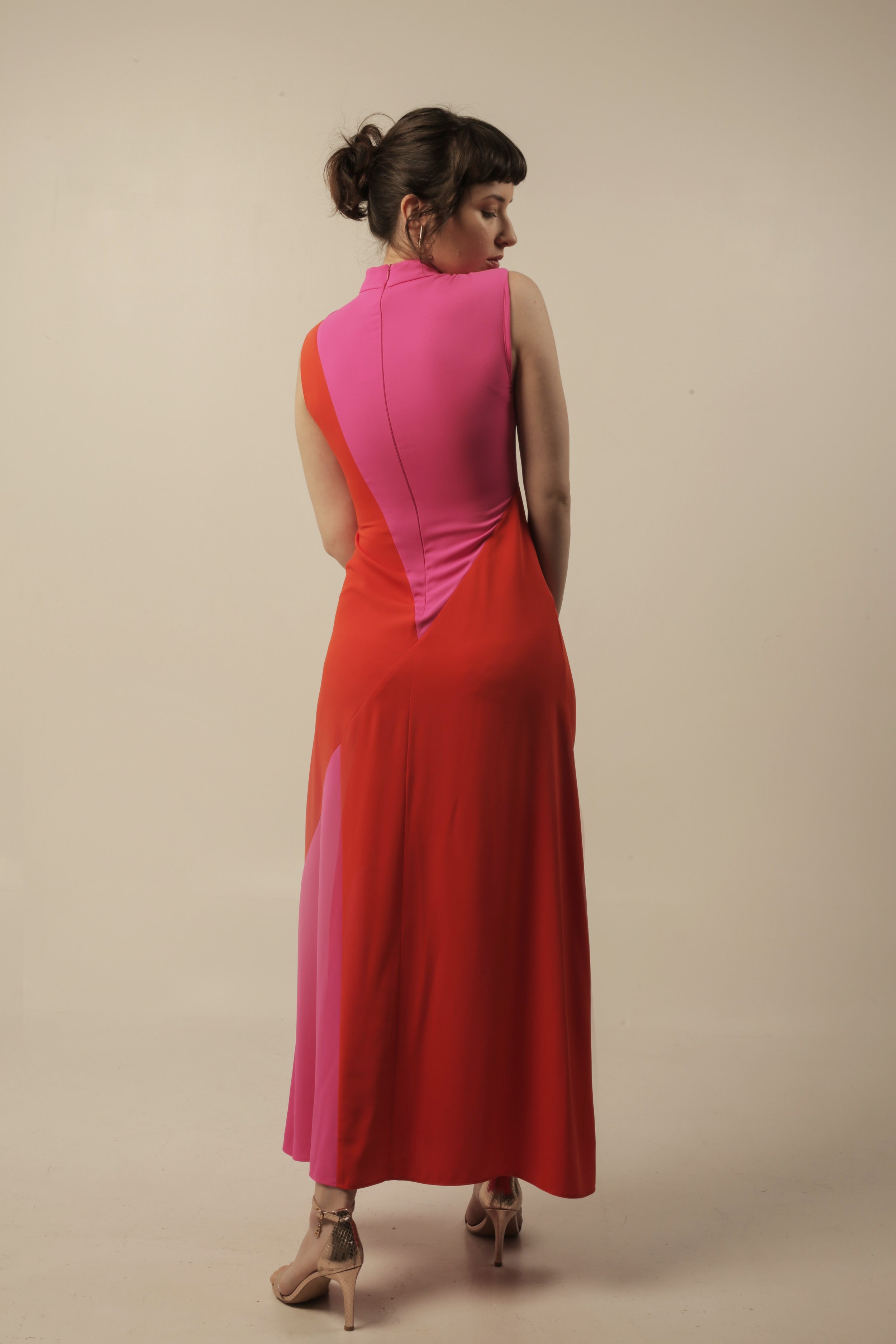 a woman in a colorful sleeveless dress standing against a plain light-colored background, looking to her right