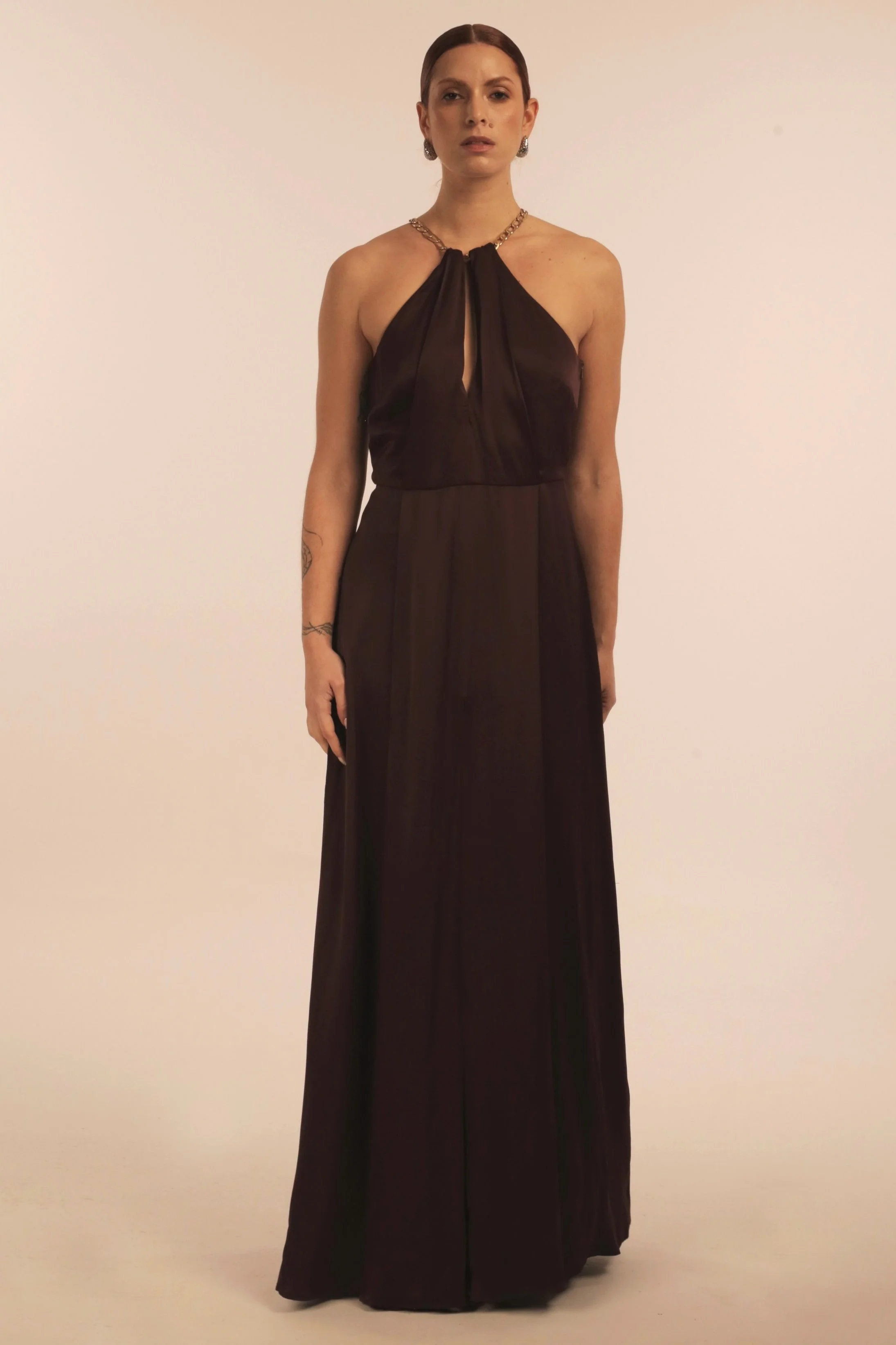 Woman wearing a long black halter dress with a keyhole cutout at the neckline, standing against a plain background.