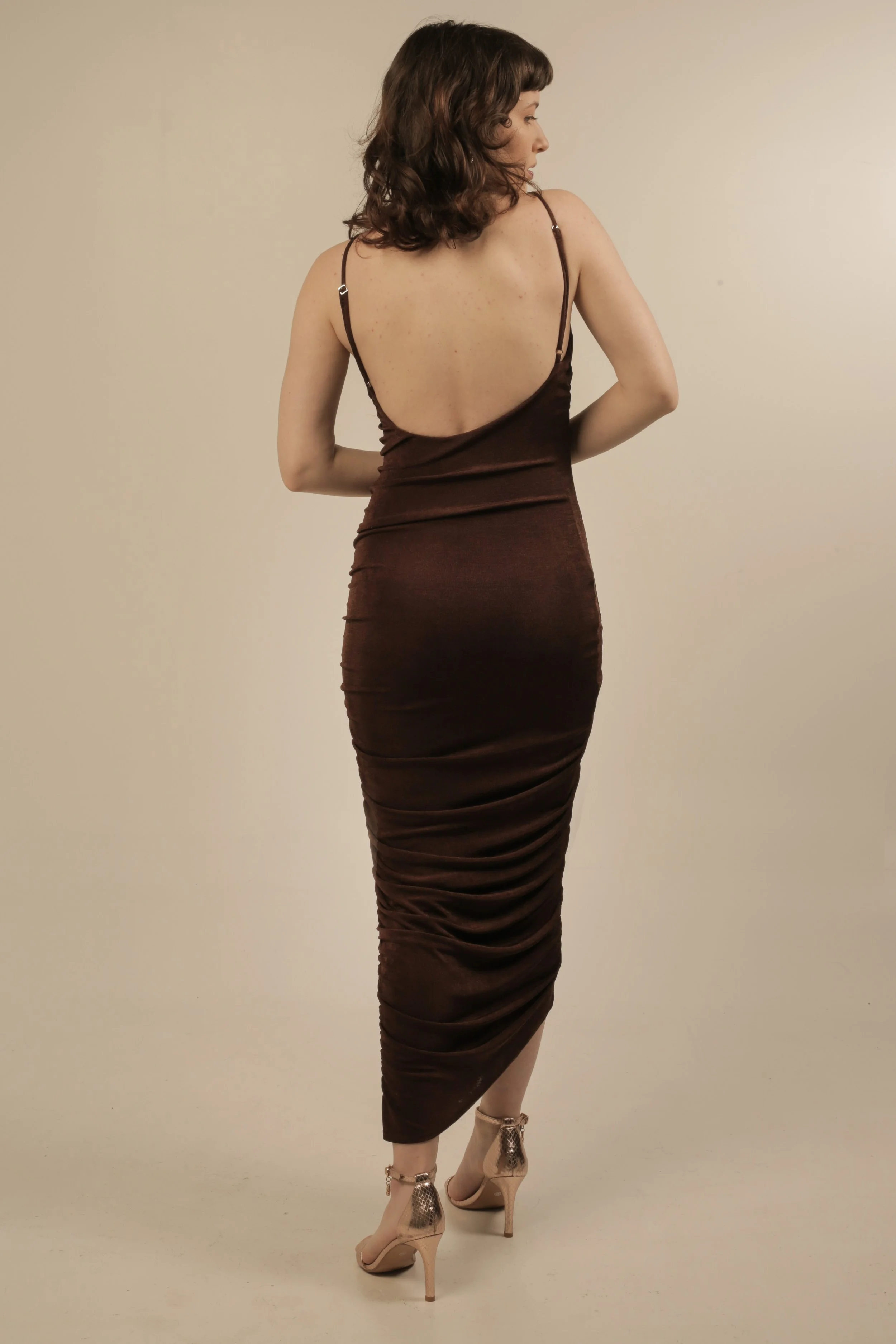 Back view of a woman in a brown, backless, fitted dress and high heels.