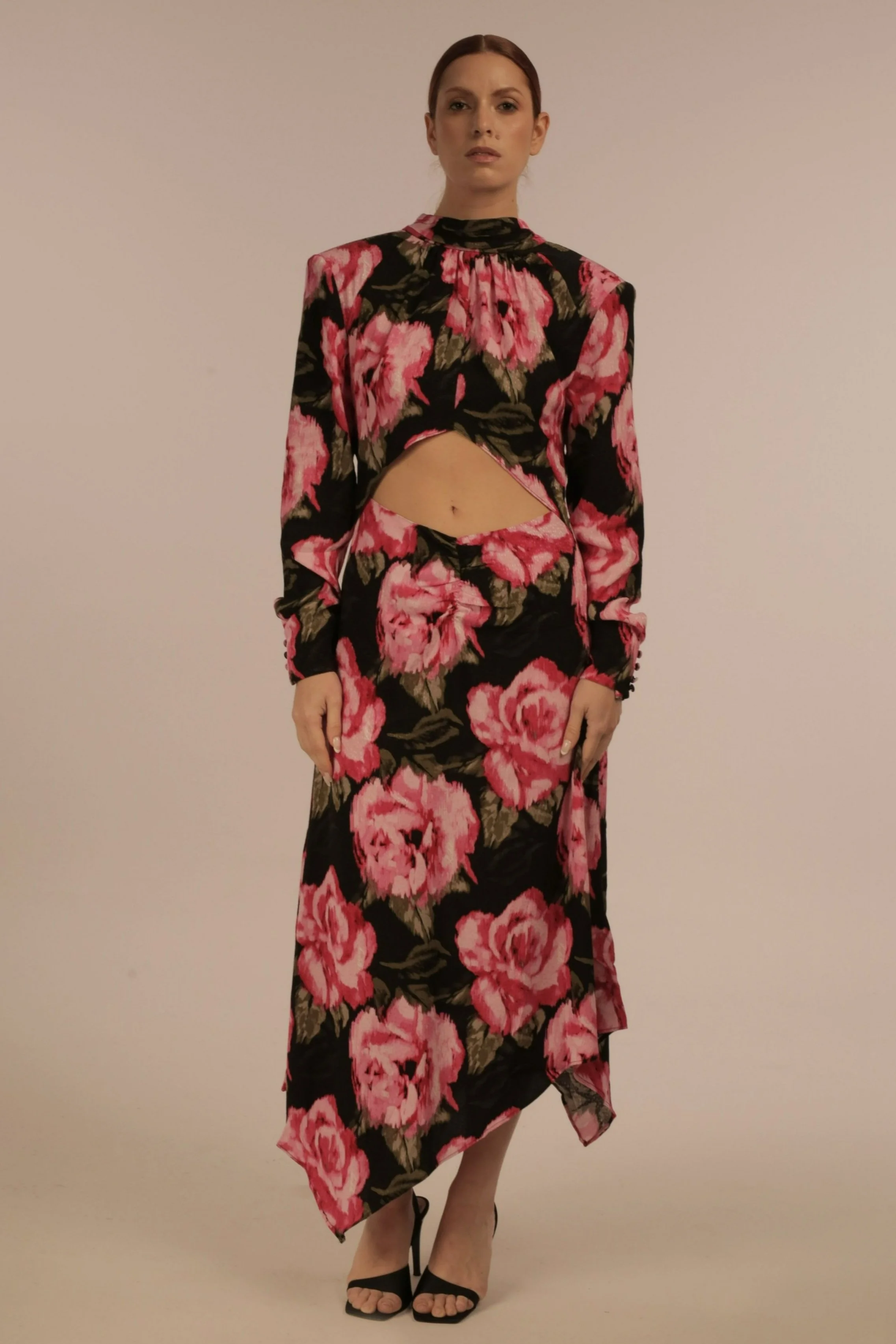 A woman wearing a black dress with a large pink floral pattern, an asymmetrical skirt, and a cutout revealing her midriff.