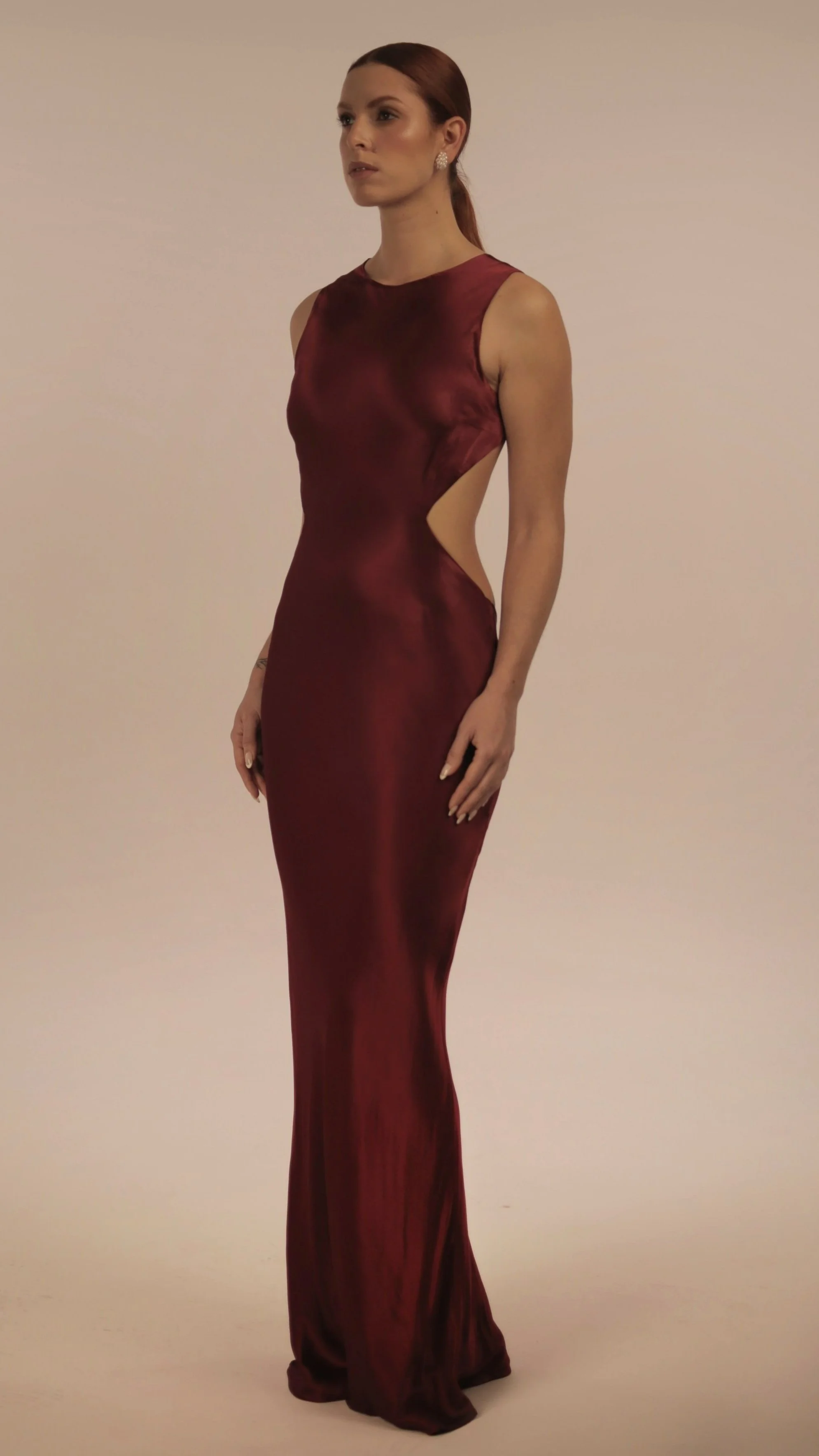 Woman with red hair in a sleek, satin, sleeveless, floor-length burgundy gown with side cutouts