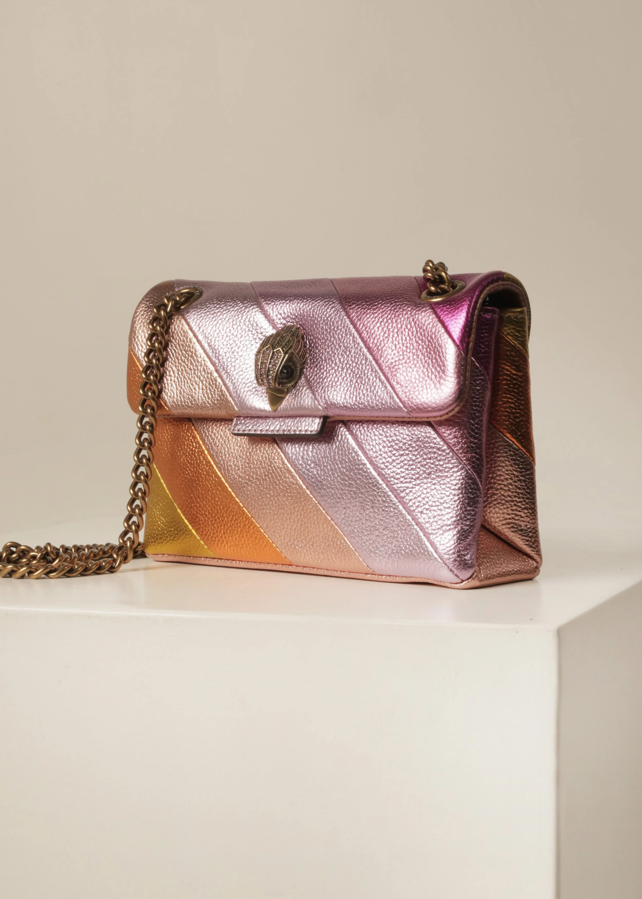 A metallic, rainbow-colored handbag with gold chain strap and a snake-shaped clasp, placed on a white surface.