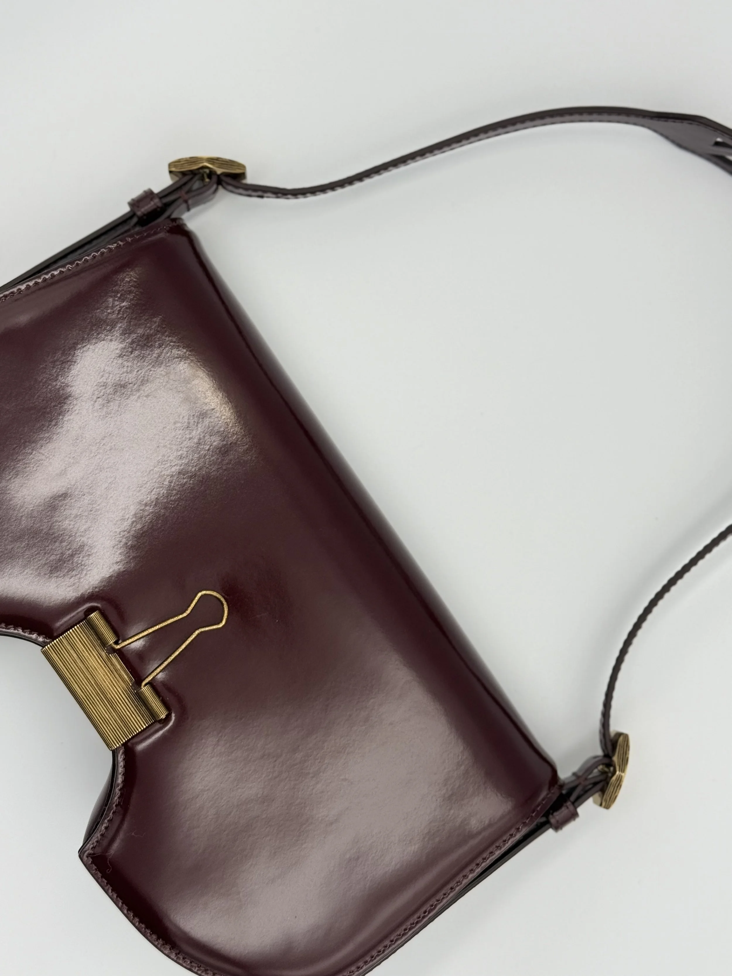 Close-up of a burgundy leather handbag with gold hardware on a white surface.
