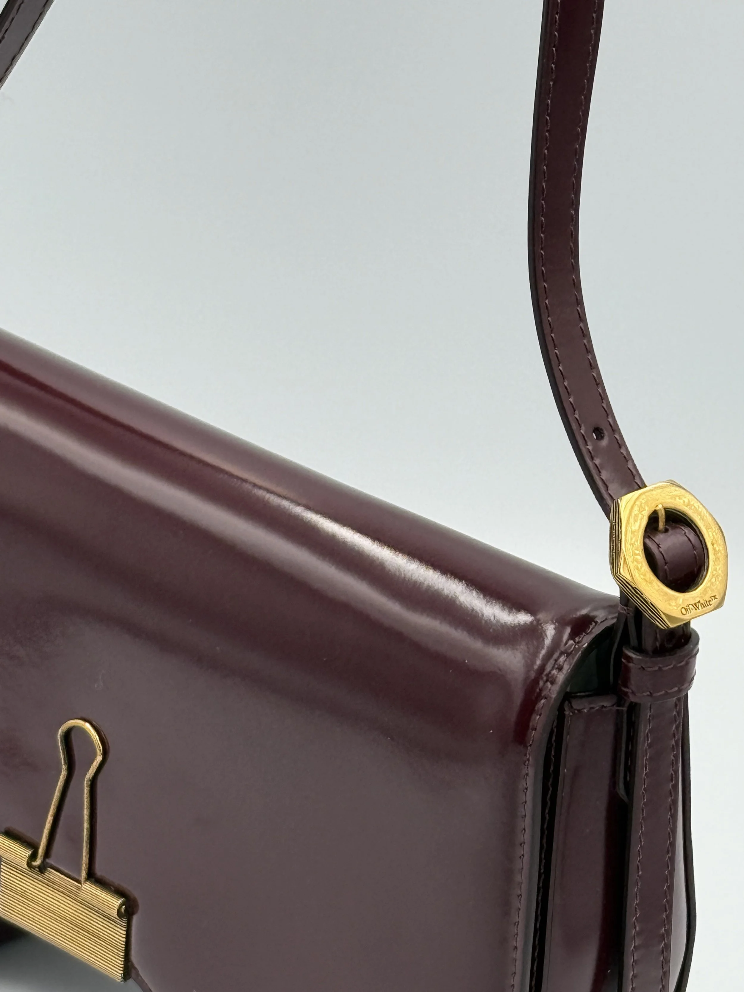 Close-up of a maroon handbag with gold hardware and a leather strap.