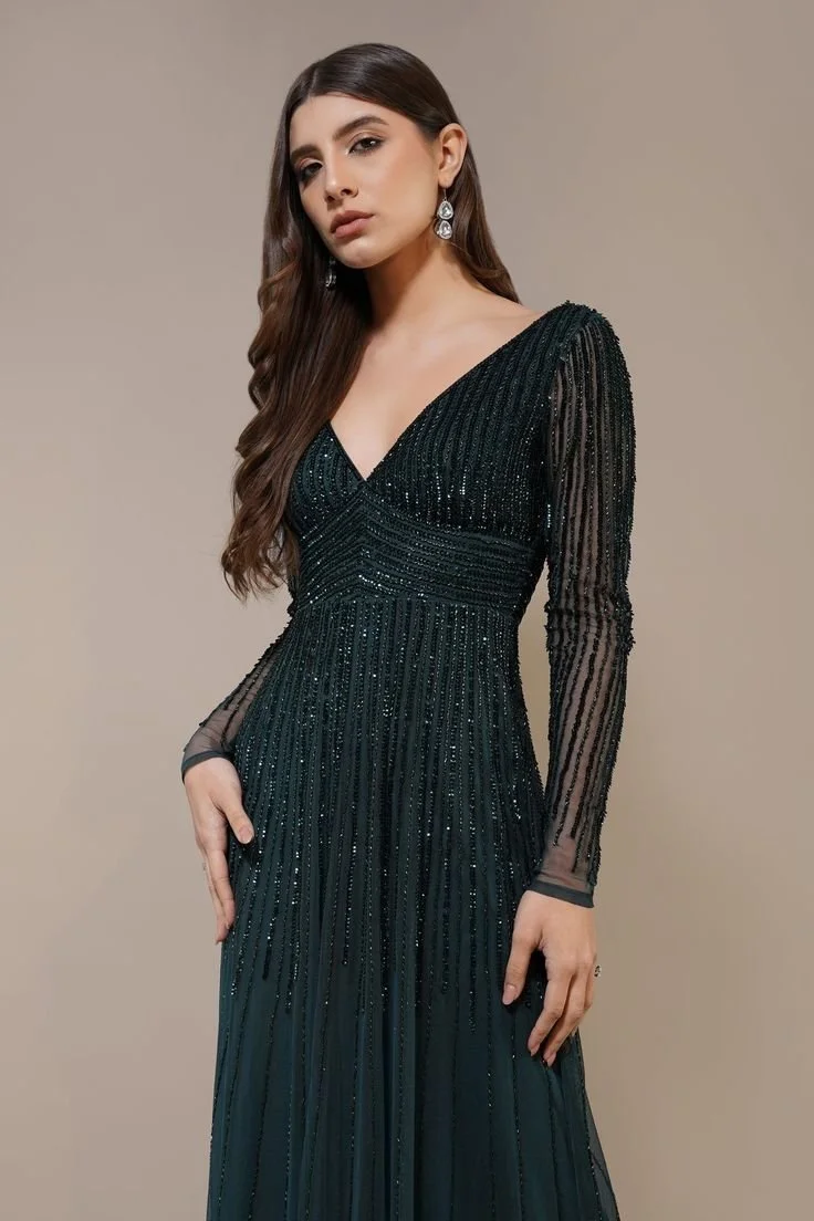 A woman with long brown hair wearing a black, long-sleeved, sparkly gown with a V-neckline, and dangling earrings.