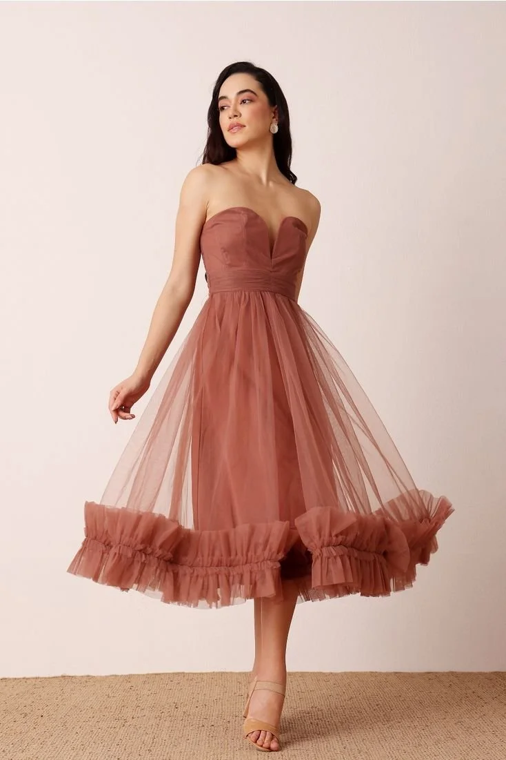 Woman wearing a strapless, rust-colored tulle dress with a ruffled hem, standing against a plain background.