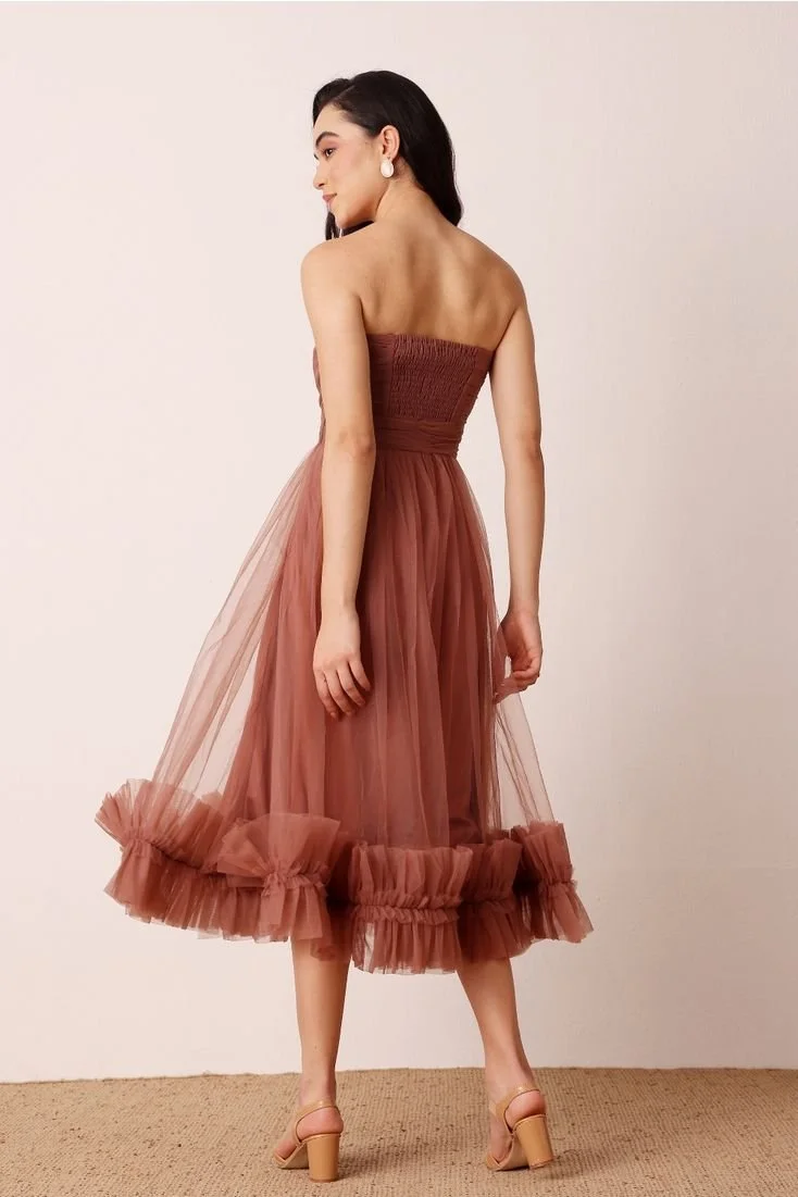 A woman wearing a strapless, brownish-pink tulle dress with ruffled hem, standing sideways against a plain background.