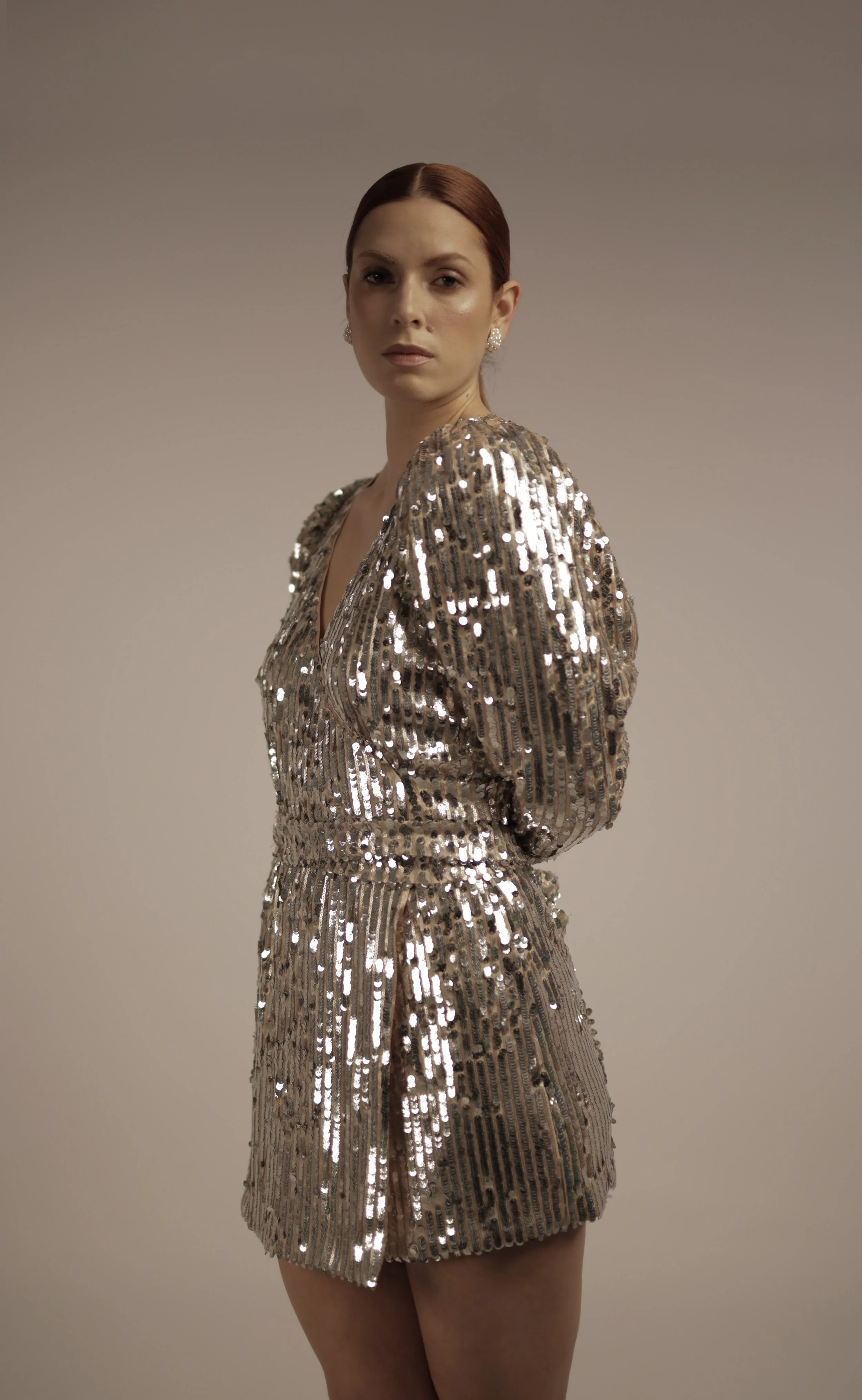Woman in a gold sequin dress standing against a neutral background.