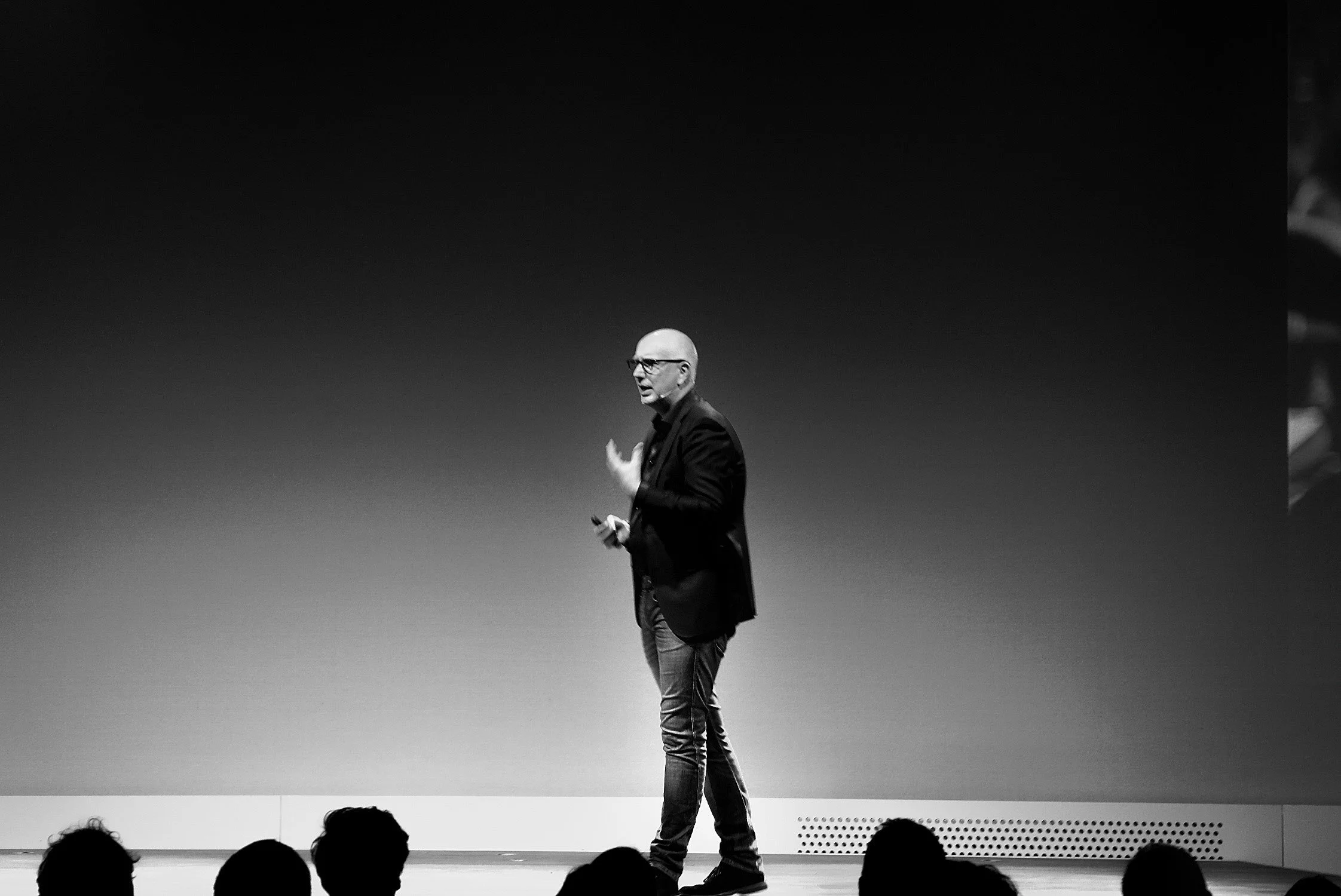 Zwart-witte foto van een man in een pak die op een podium spreekt voor een publiek.