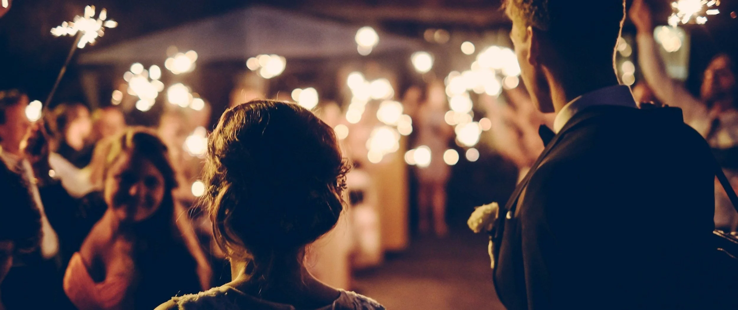 Grand exit of beautiful couple at night with wedding guests holding sparklers.