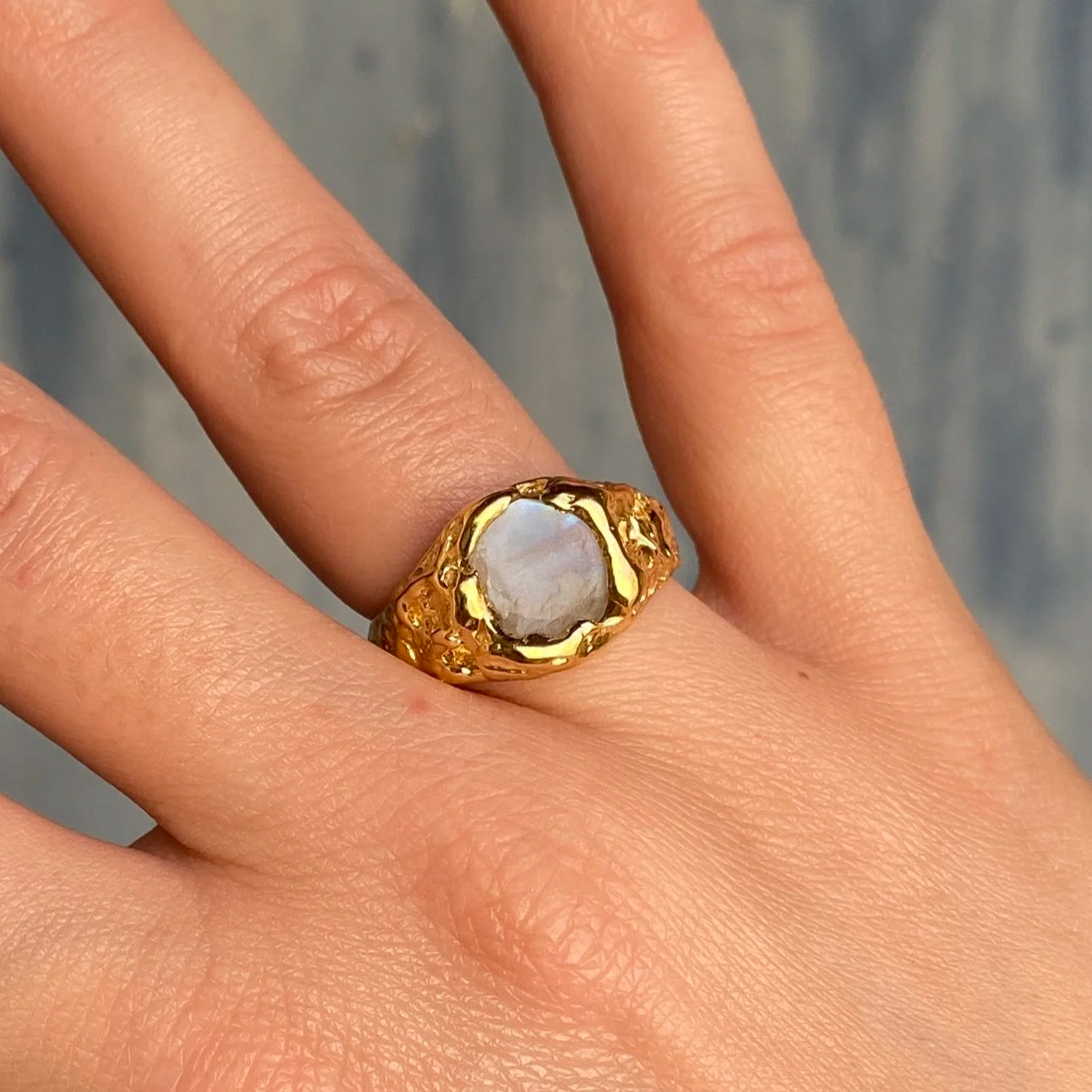 Bague en or avec une pierre d'opale blanche sur le doigt d'une main.