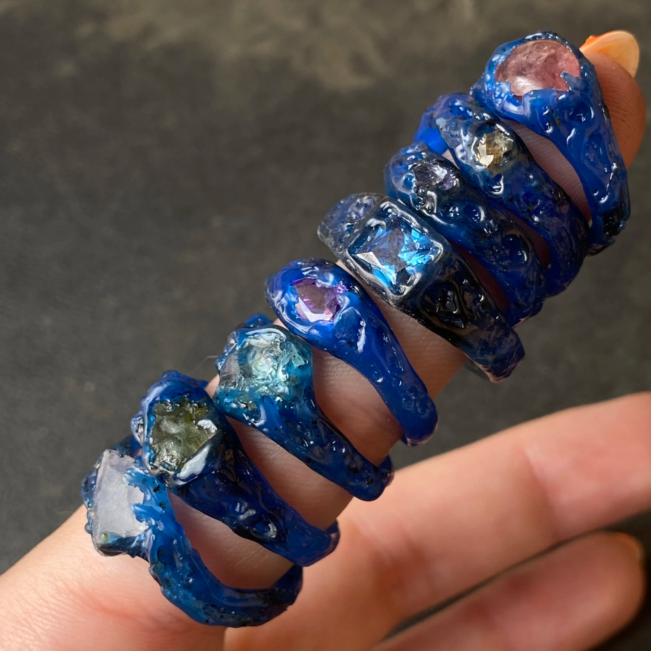 Une main portant plusieurs bagues en résine bleue avec des pierres colorées intégrées.