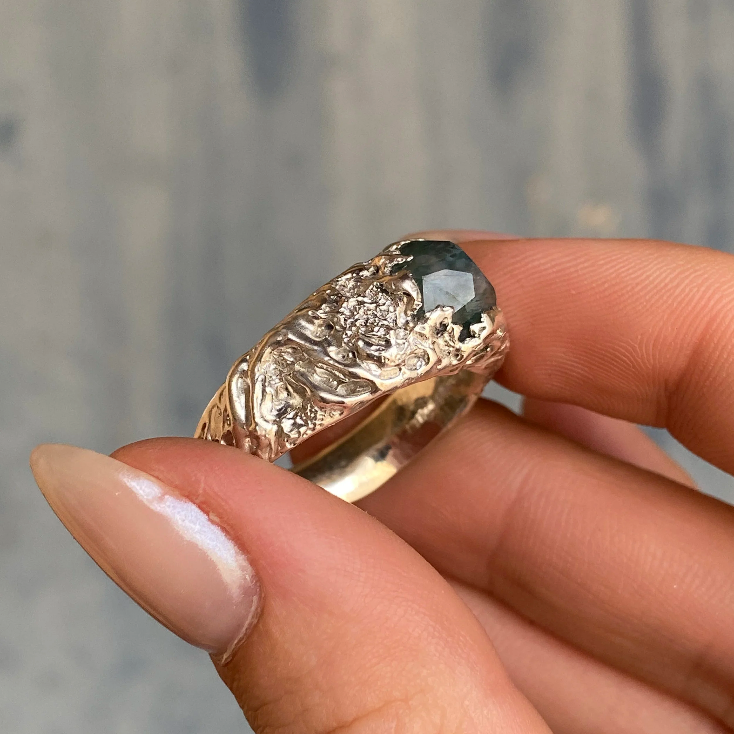 Une bague en or ornée d'une pierre sombre facettée, avec une surface décorative complexe en relief.