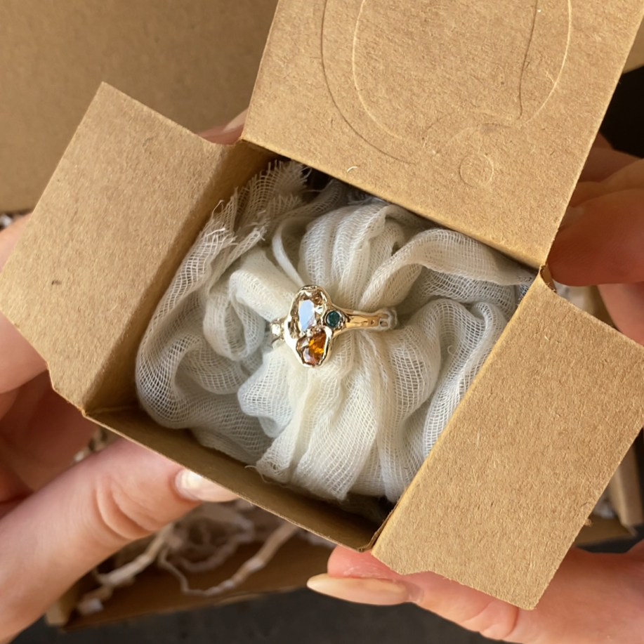 Une bague avec des pierres colorées dans une boîte en carton.