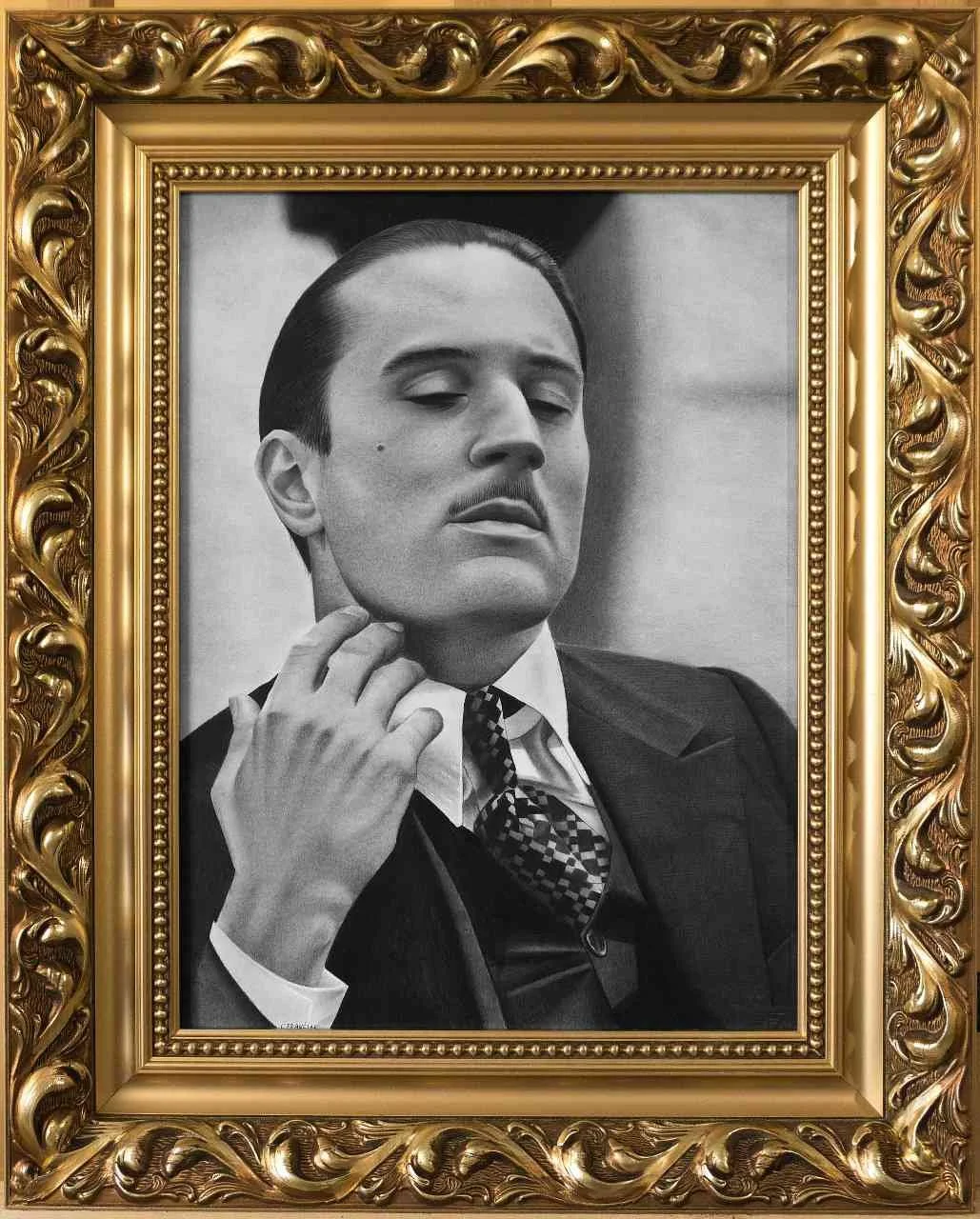 Black and white portrait of a man in a suit with a patterned tie, posed with one hand touching his neck, framed with an ornate gold frame.