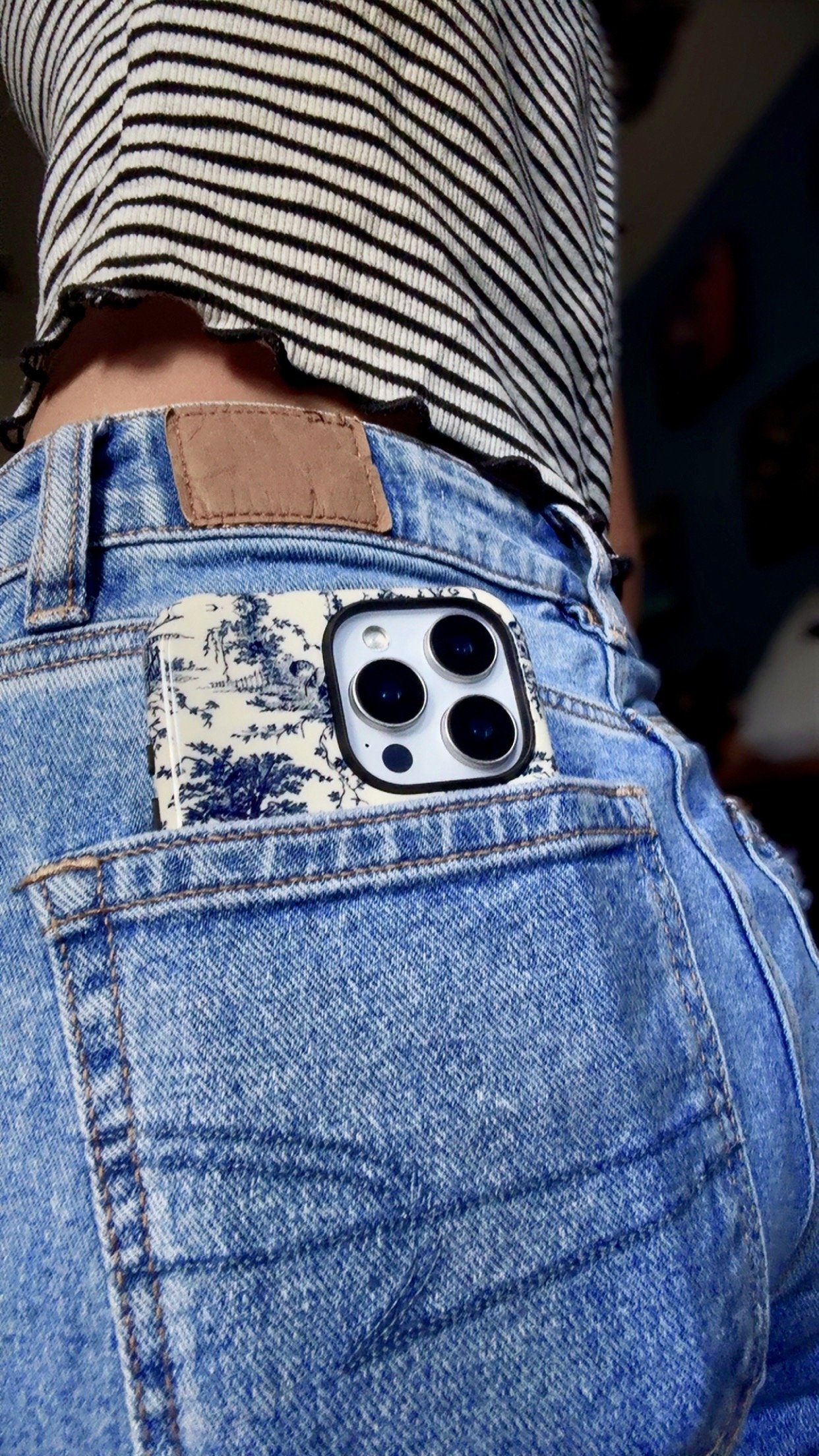 Close-up of a smartphone with a blue and white tapestry pattern case, partially visible in the back pocket of blue jeans.