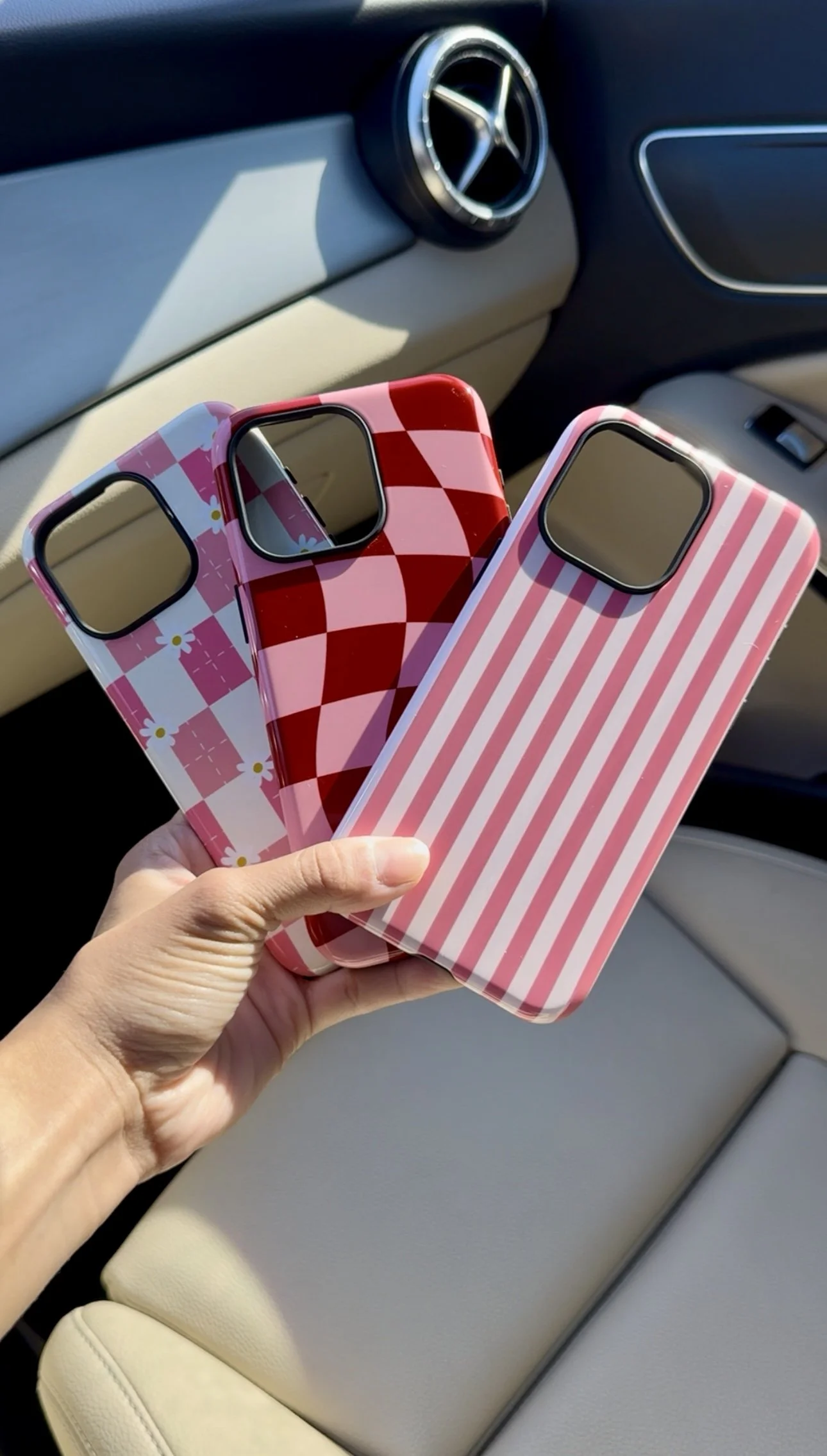 Person holding three colorful striped and patterned phone cases inside a car.
