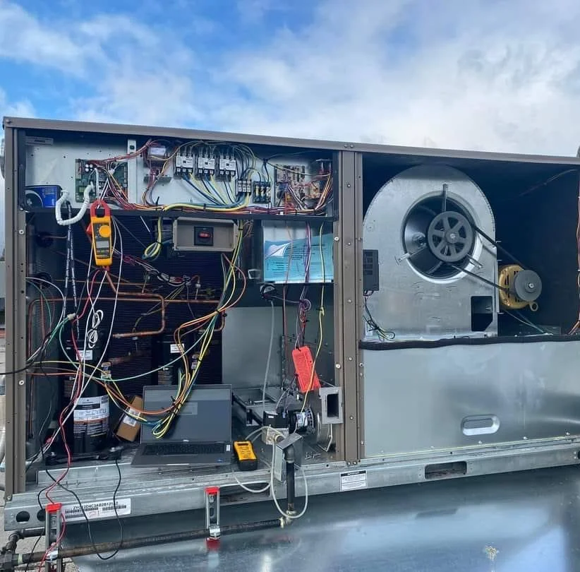Open HVAC unit with exposed wiring, electrical components, and fan motor inside the metal casing.