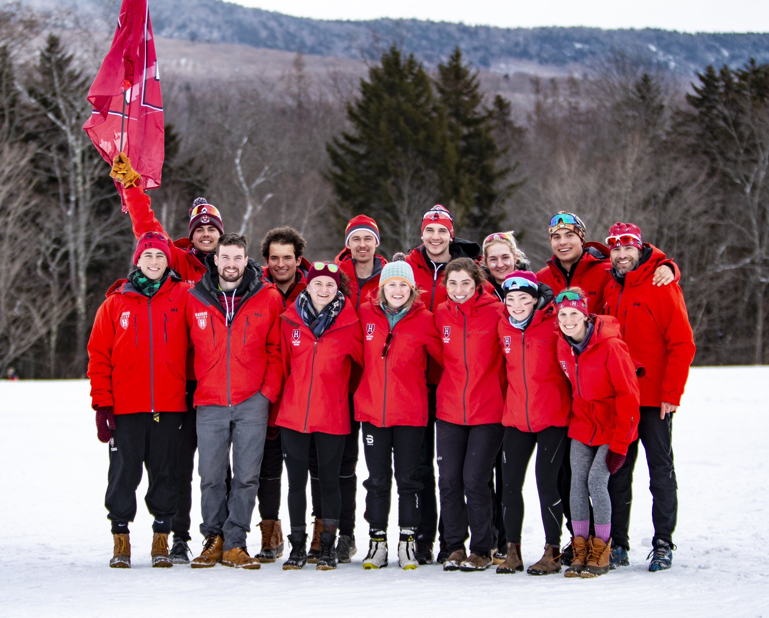 Group of people wearing red jackets on snow, with one holding a red flag, standing in a winter landscape.