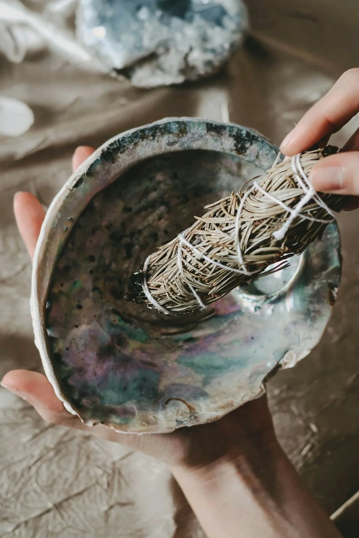 Person holding a large clam shell with a bundle of burning sage inside.