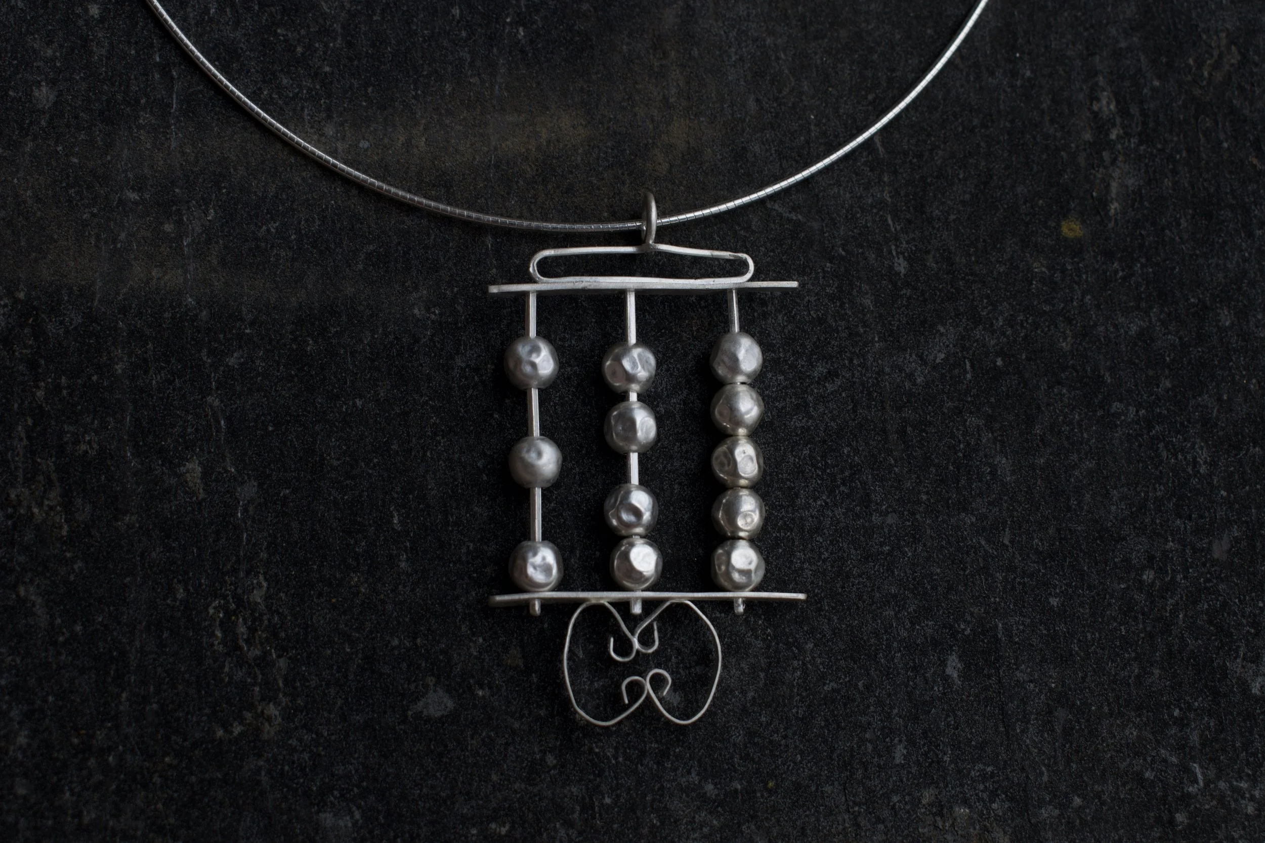 Silver jewelry necklace with pendant and dangling beads on a dark textured background.